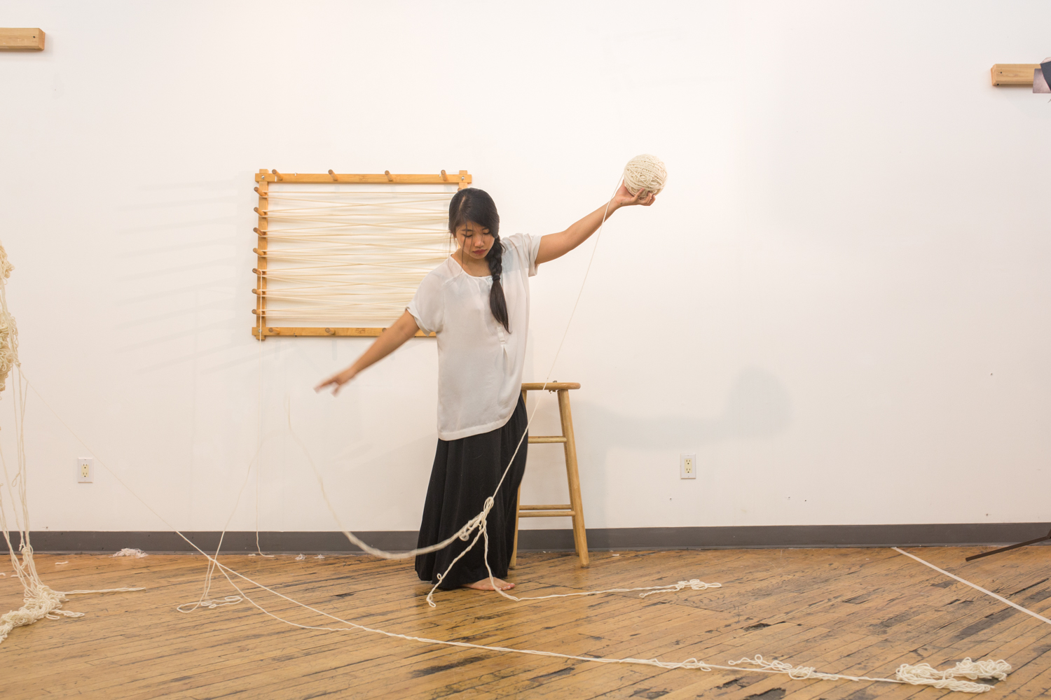 Artist throws the strand of untangled yarn onto the floor with her right hand as she lifts up the ball of untangled yarn with her left hand.