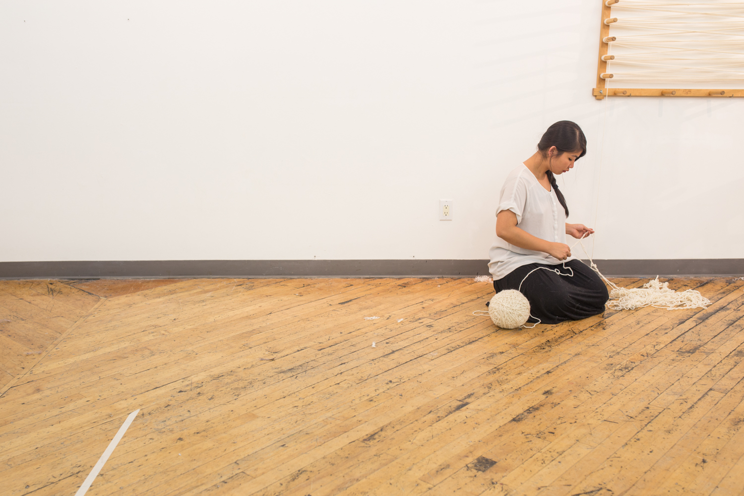 The artist kneels on the floor to untangle a knot. The ball of untangled yarn is almost at 8 inches in diameter.