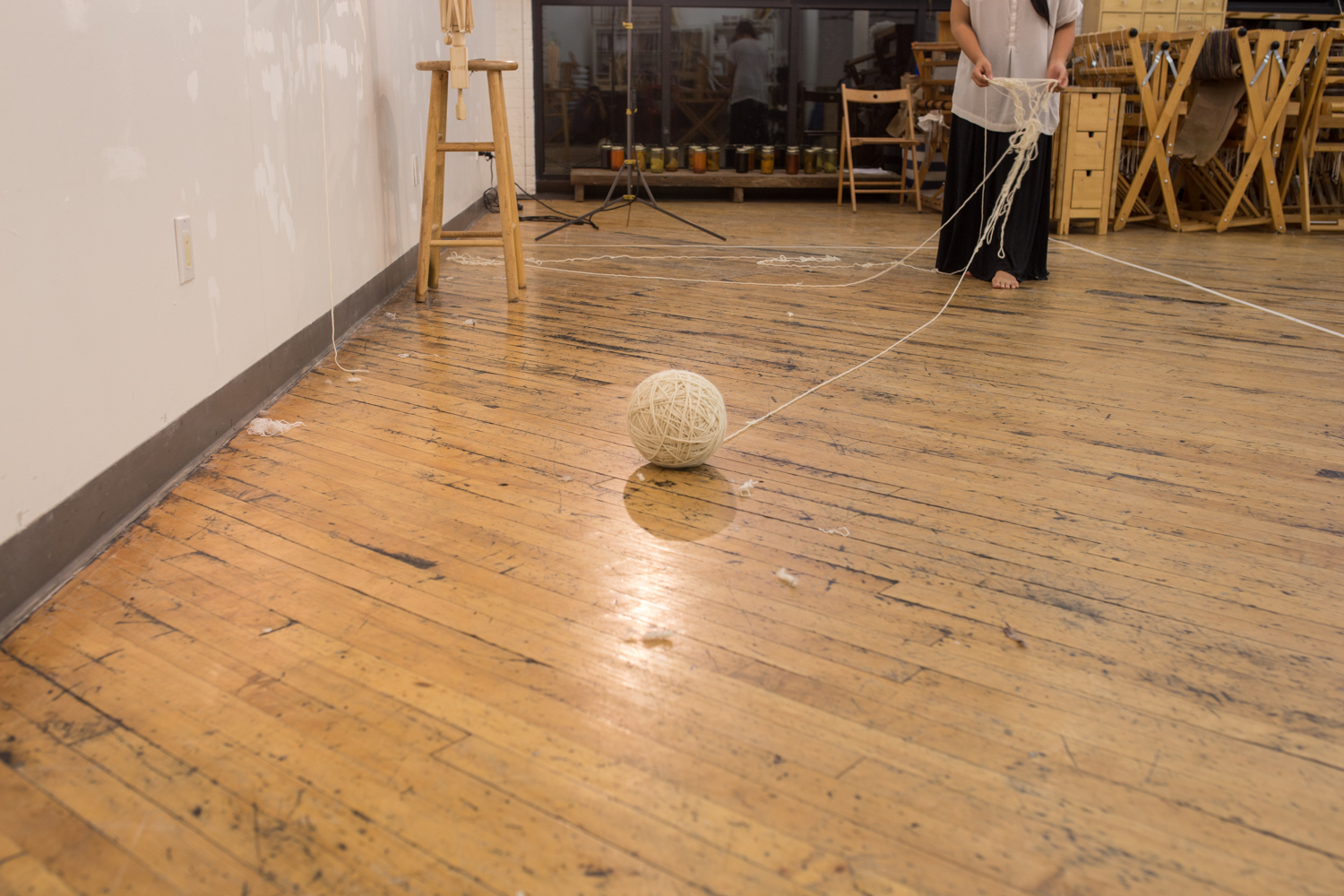 A large ball of untangled yarn is in the foreground. It’s now around 9 inches in diameter. the artist is in the background untangling a small strand of knotted yarn.
