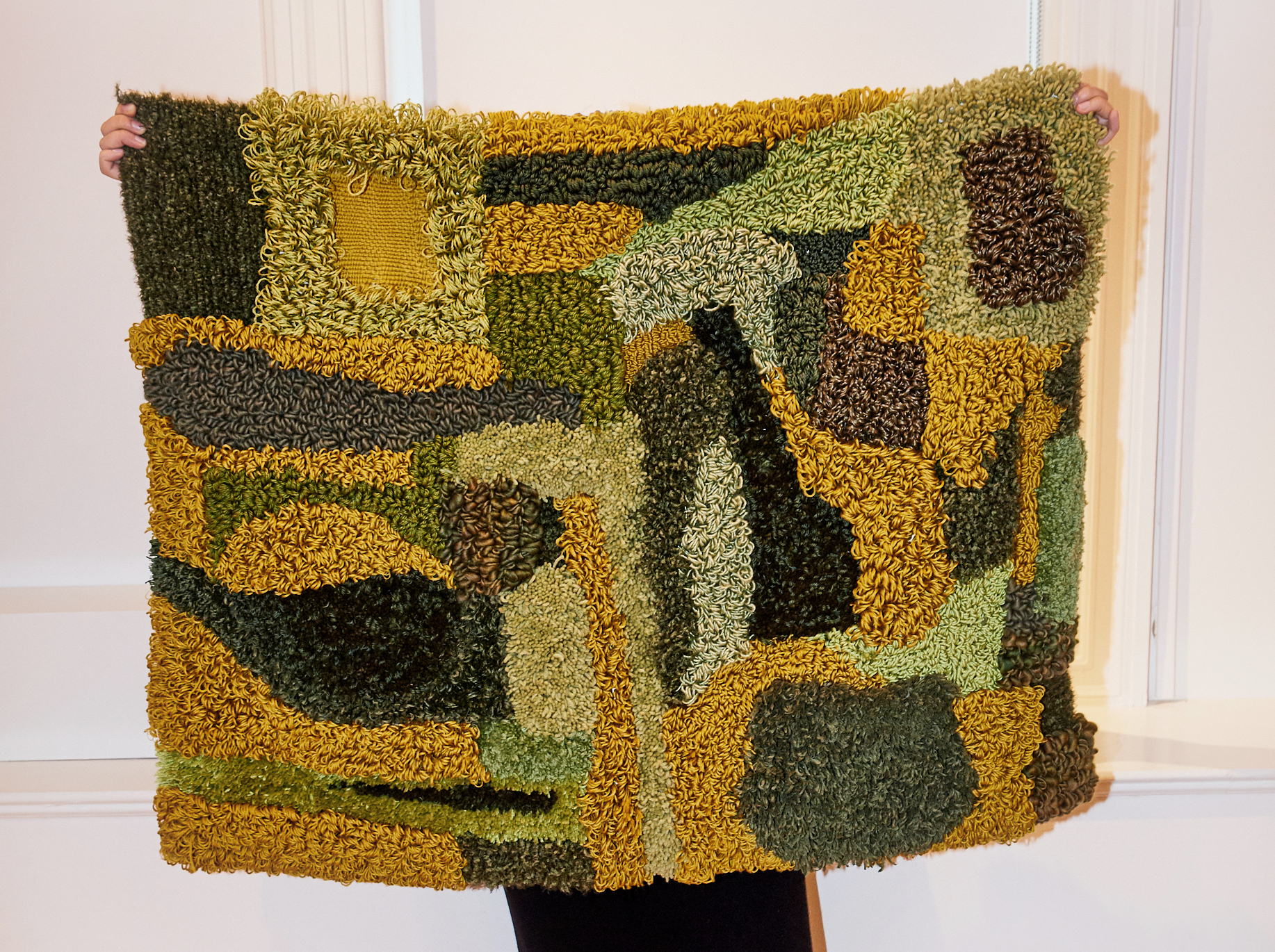 The artist holding up the rug against a window sill to completely cover her face.