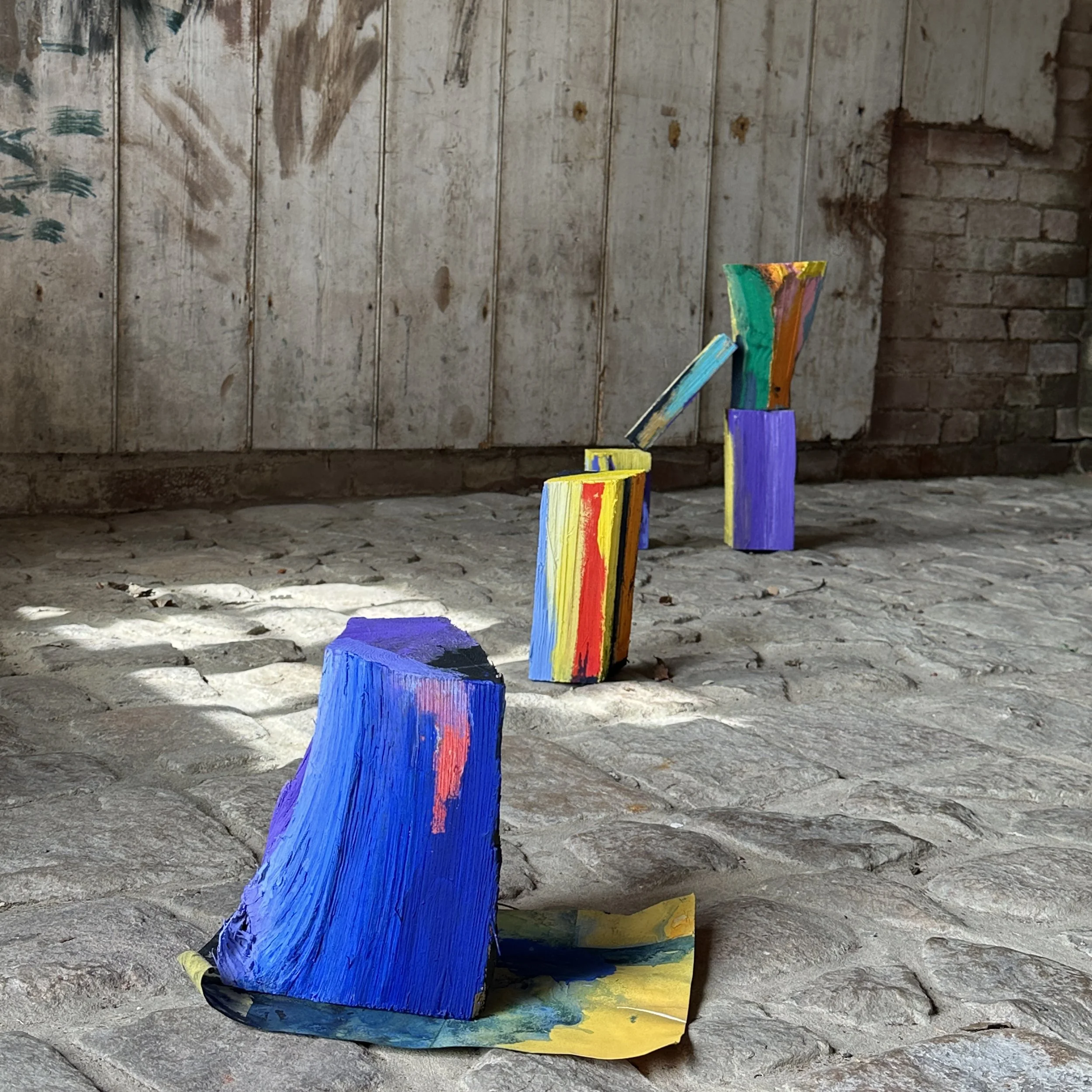 Painted wooden blocks arranged in a line on a cobblestone floor, with a rustic wall background.