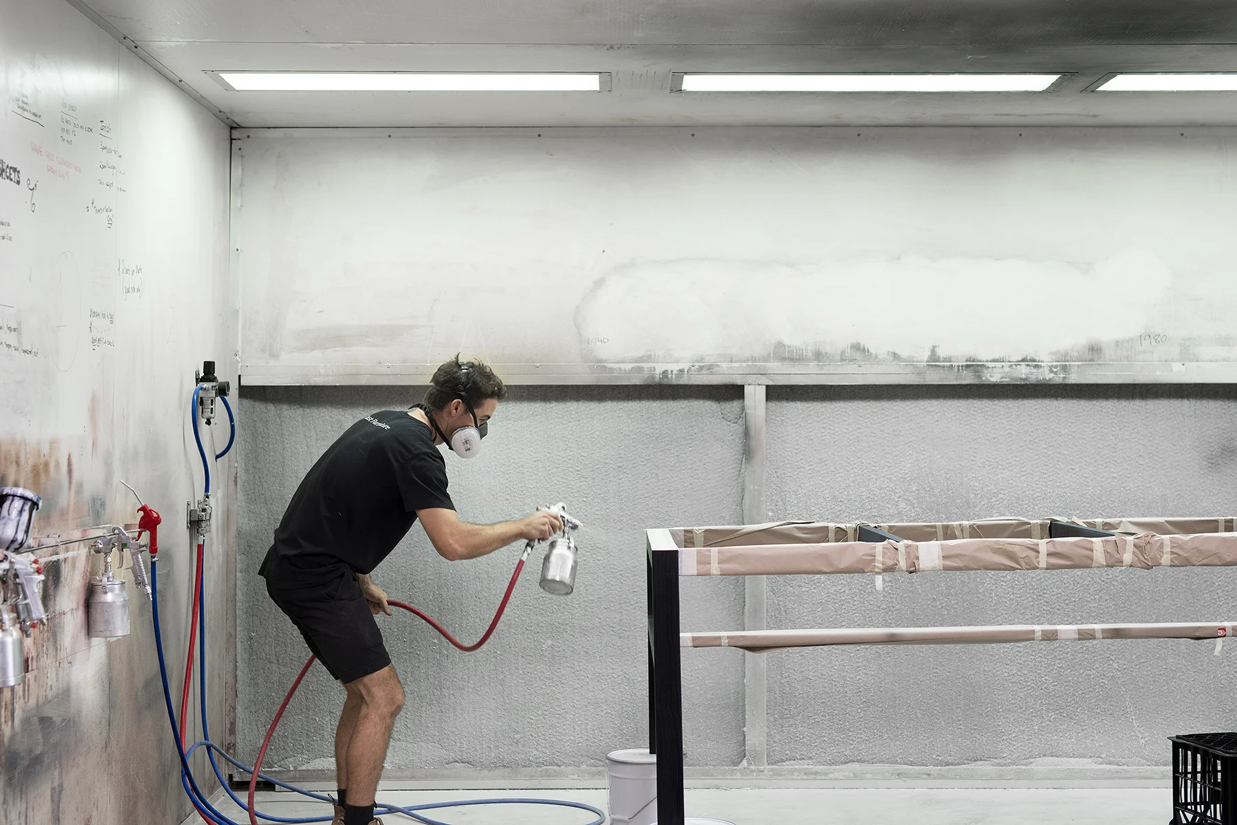 The spraybooth is located in the middle of the workshop. Rory spays a coat of colour onto a Willox table frame to stain the wood. The table will then need to be sanded and another coat of colour applied.