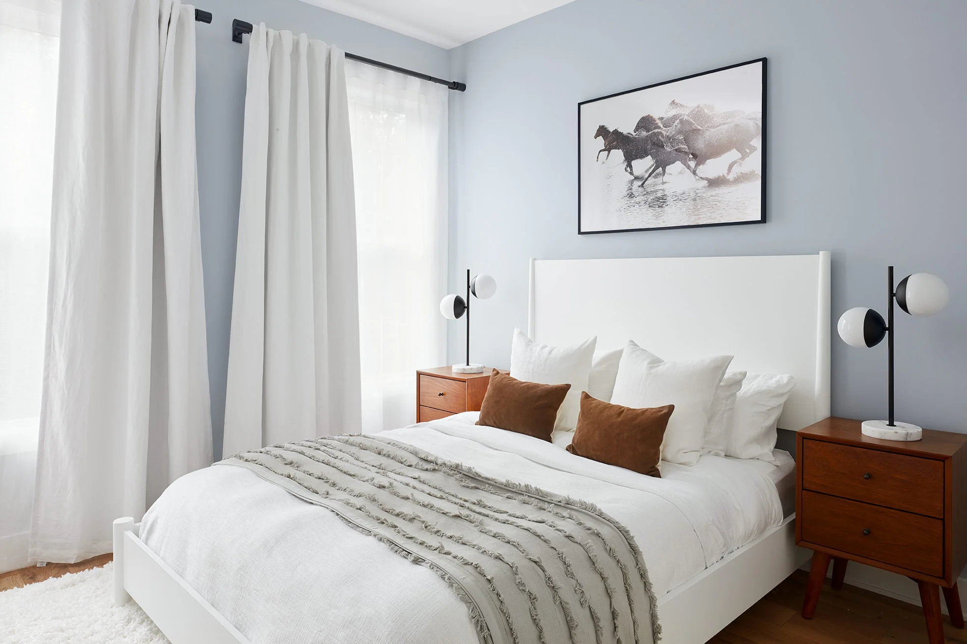 The second bedroom has the same headboard as the first but in white, to keep the spaces cohesive. Warm wood nightstands and brown suede pillows add contrast to the crisp white bedding and plush white rug.