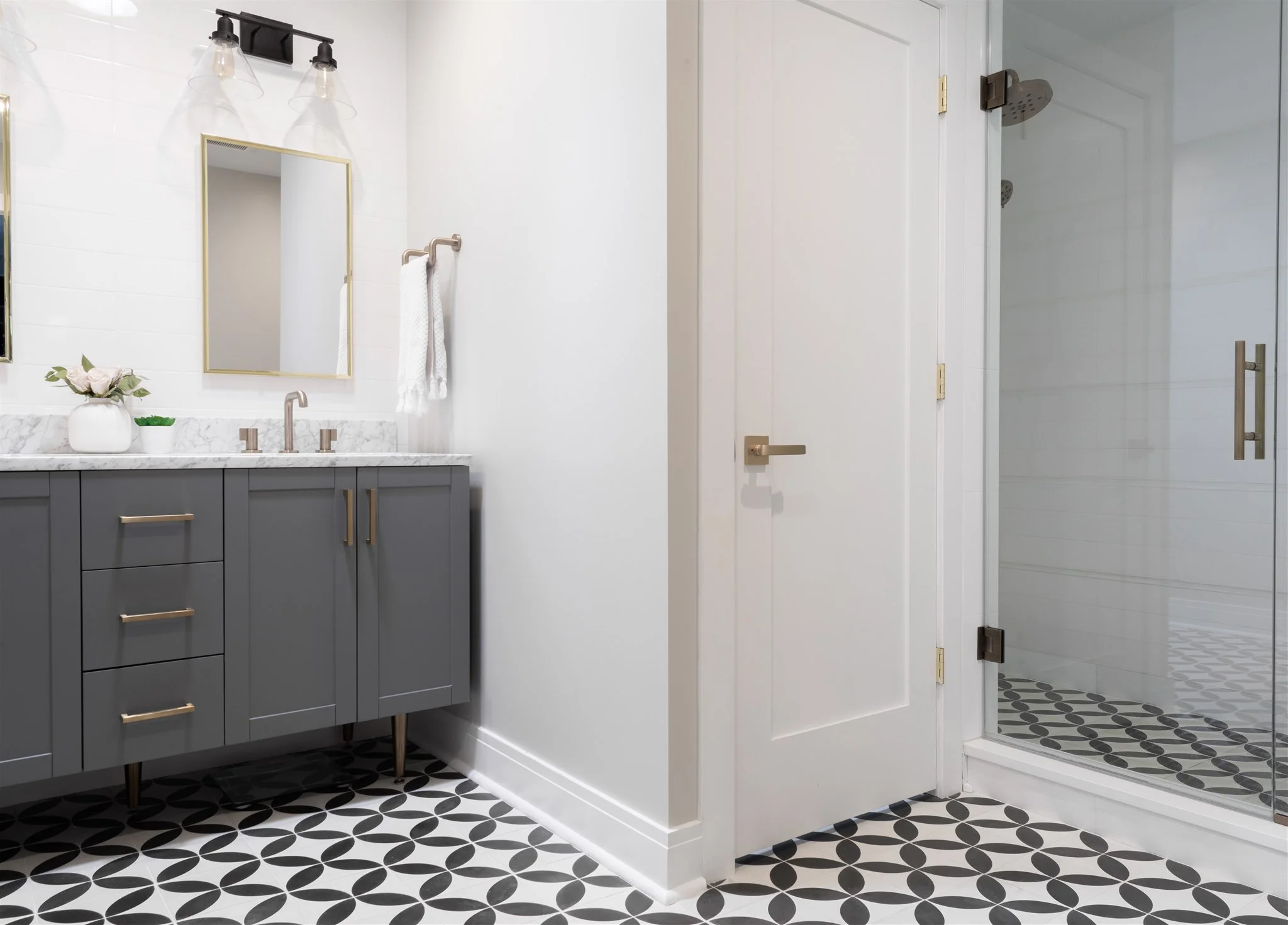 We pulled in some fun, cheerful patterns in this space to add contrast to the otherwise light and soft bathroom. The gray and marble vanity gets warmed up with brass accents, which we carried throughout the rest of the bathroom in plumbing fixtures and door hardware.