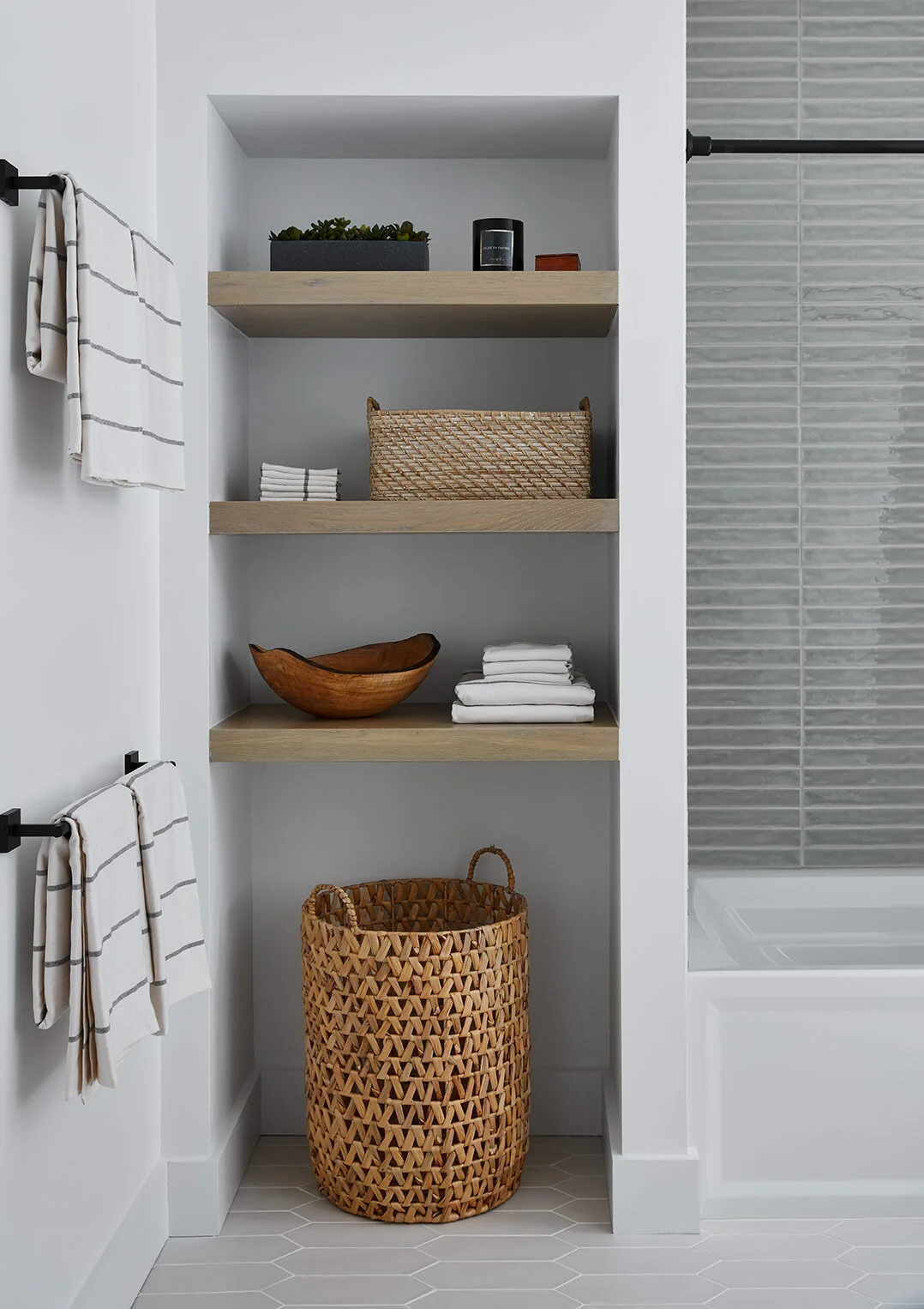 This bathroom is primarily intended for guests, so instead of a traditional linen closet, we opted for open shelving where baskets and folded towels can be placed for easy access. A hamper underneath pulls in warmth and texture to contrast the coole…