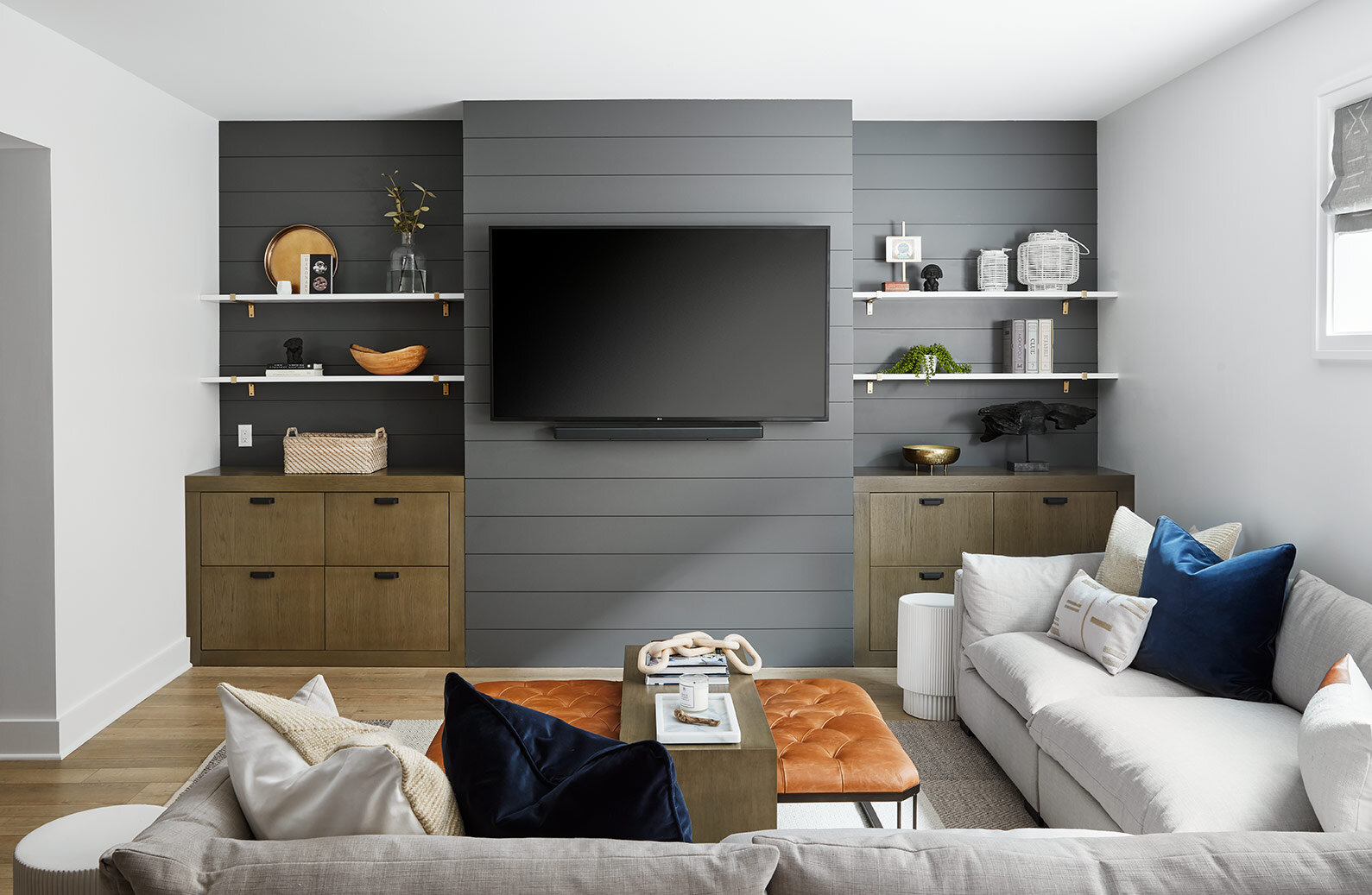 In the family room area, we added a window to the side, allowing natural light to spill in and mitigate any basement/cave-like feelings. Along the media wall, we carried in the charcoal shiplap and anchored it with built-in storage that coordinates …