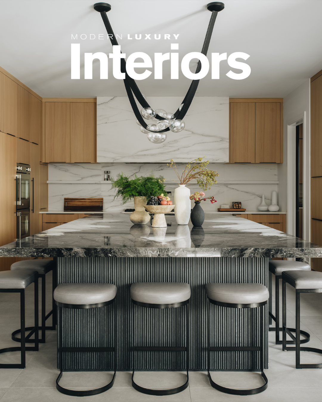 Modern luxury kitchen with marble island, wooden cabinets, black and glass chandelier, decorative vases, and flowers.