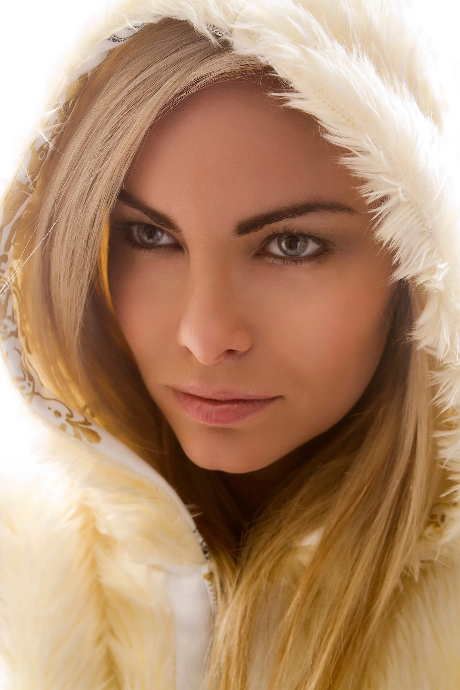 A woman with blonde hair and blue eyes wearing a hooded white furry jacket.