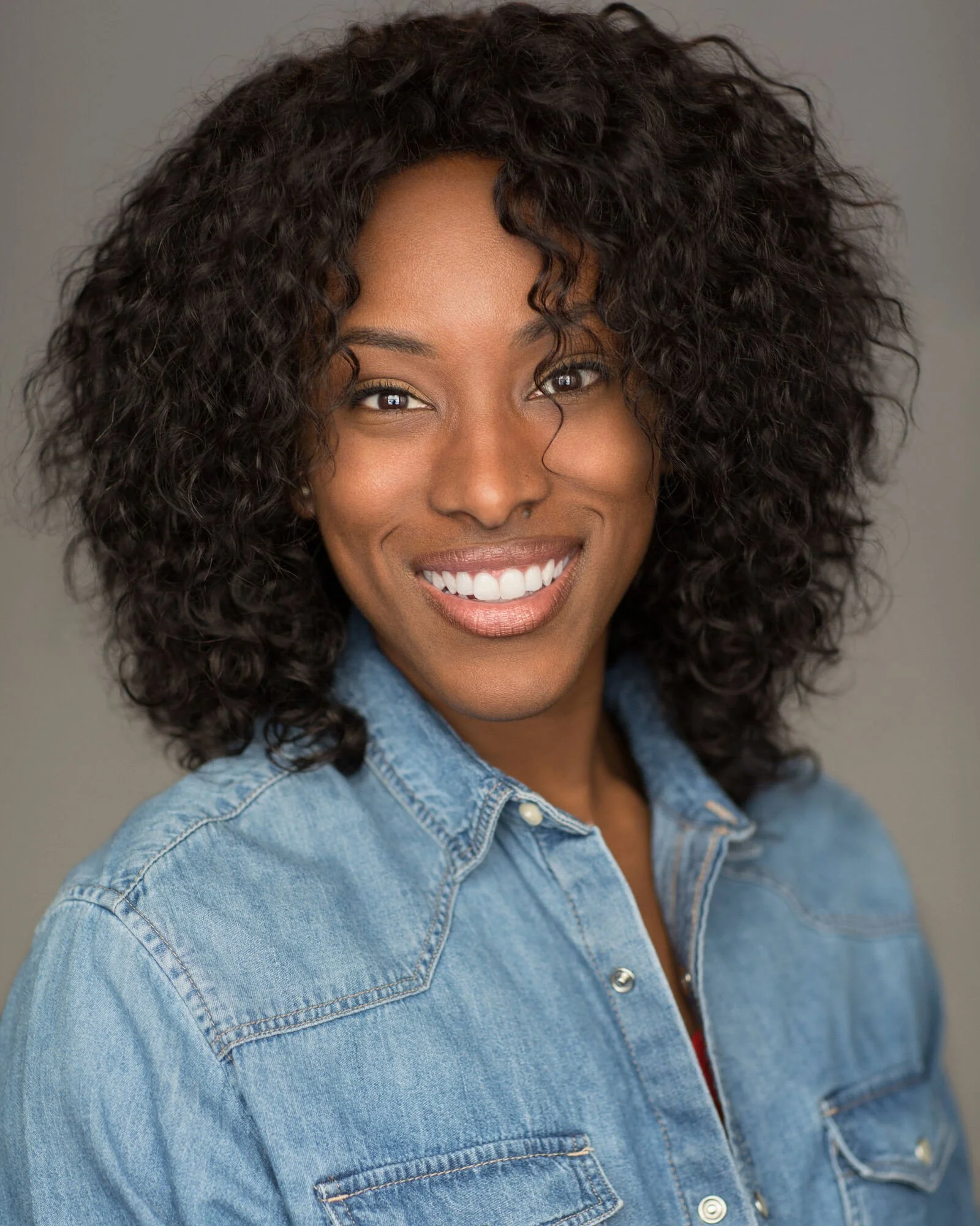 Portrait of a woman with curly hair smiling, wearing a denim shirt