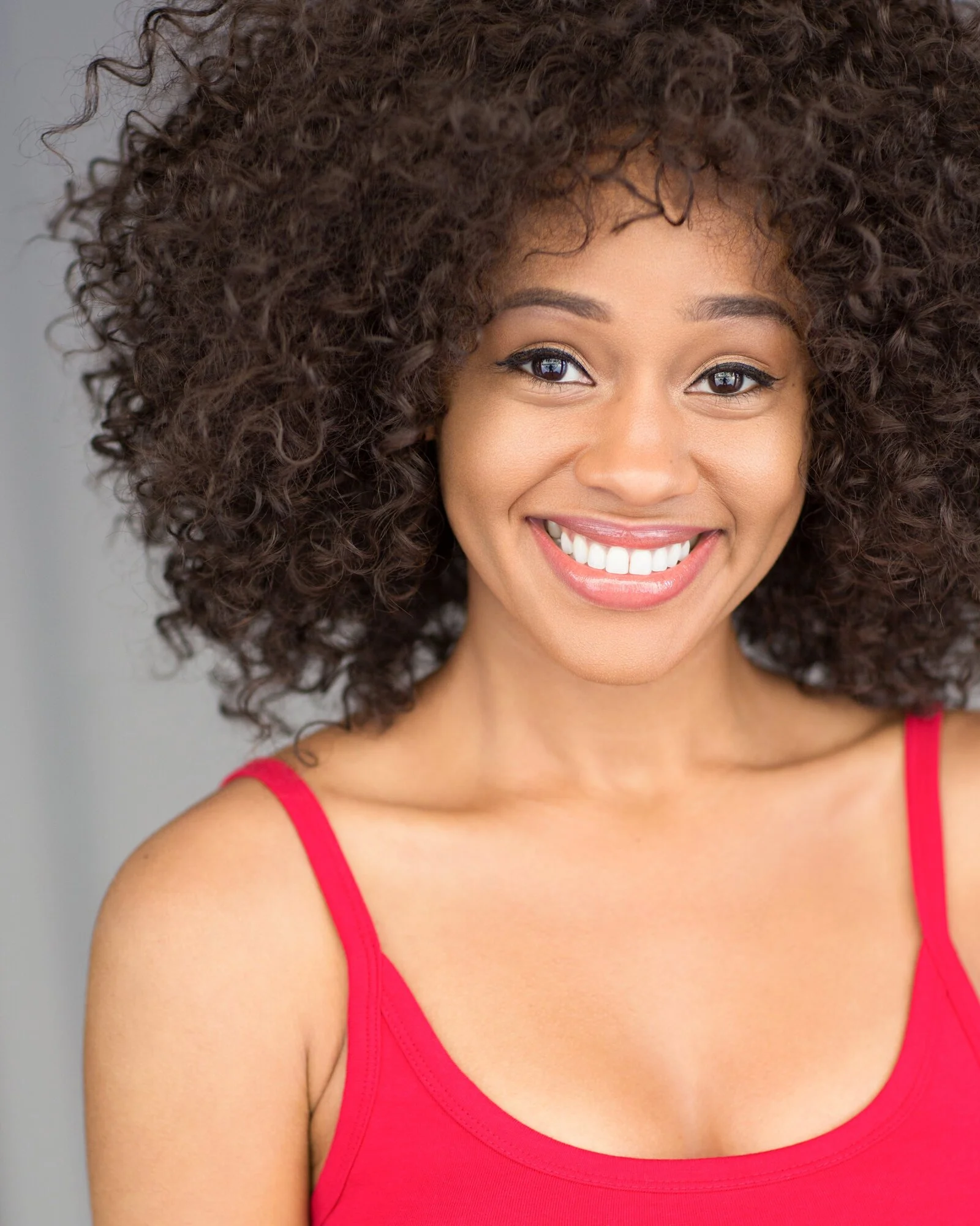 A woman with curly hair smiling and wearing a red tank top.