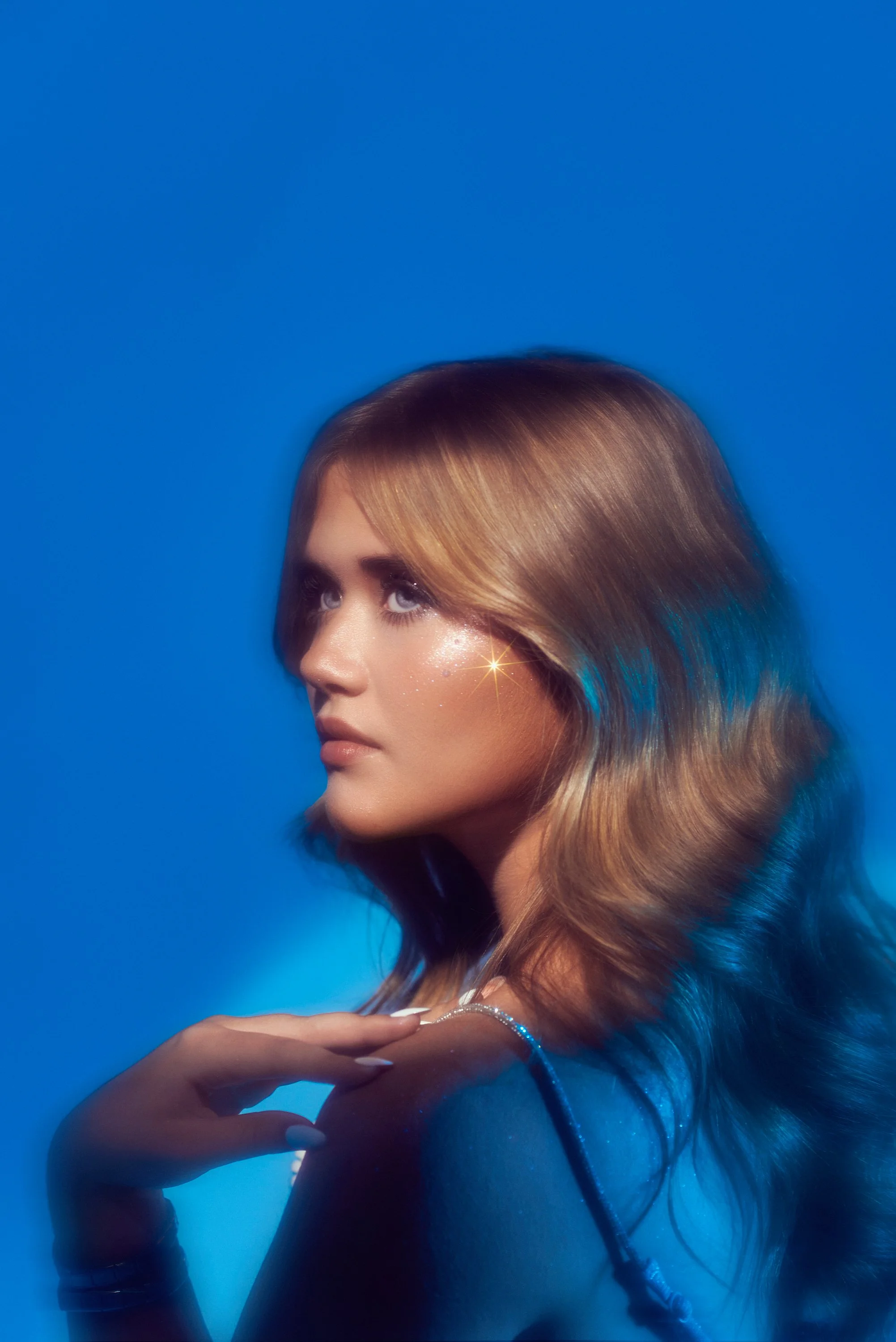 Retrato de una mujer con cabello rubio, resaltada por luz brillante y fondo azul.