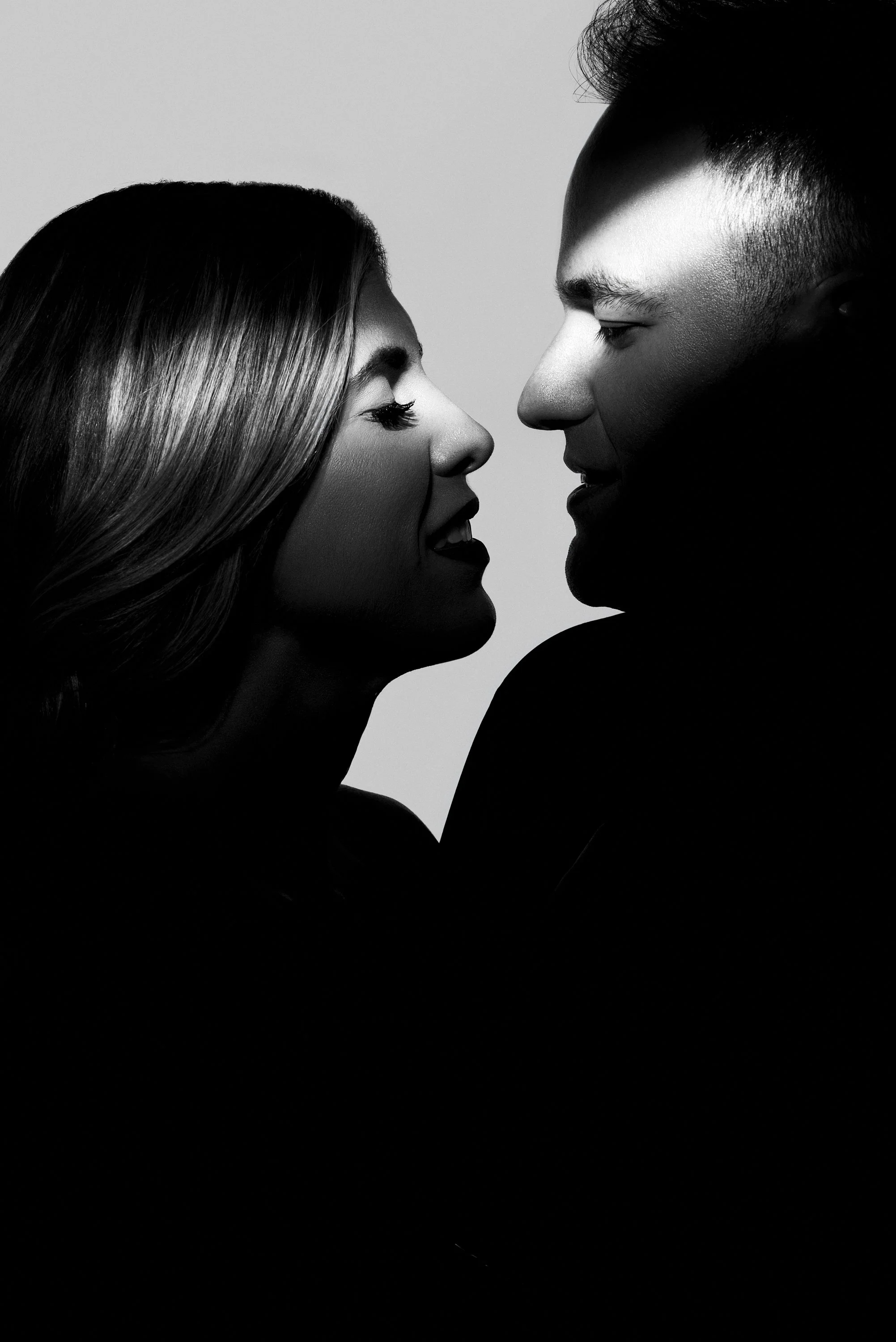 Un primer plano en blanco y negro de una pareja, hombres y mujeres, mirando cuidadosamente y acercándose con las narices casi tocándose, en un estilo de fotografía artística.
