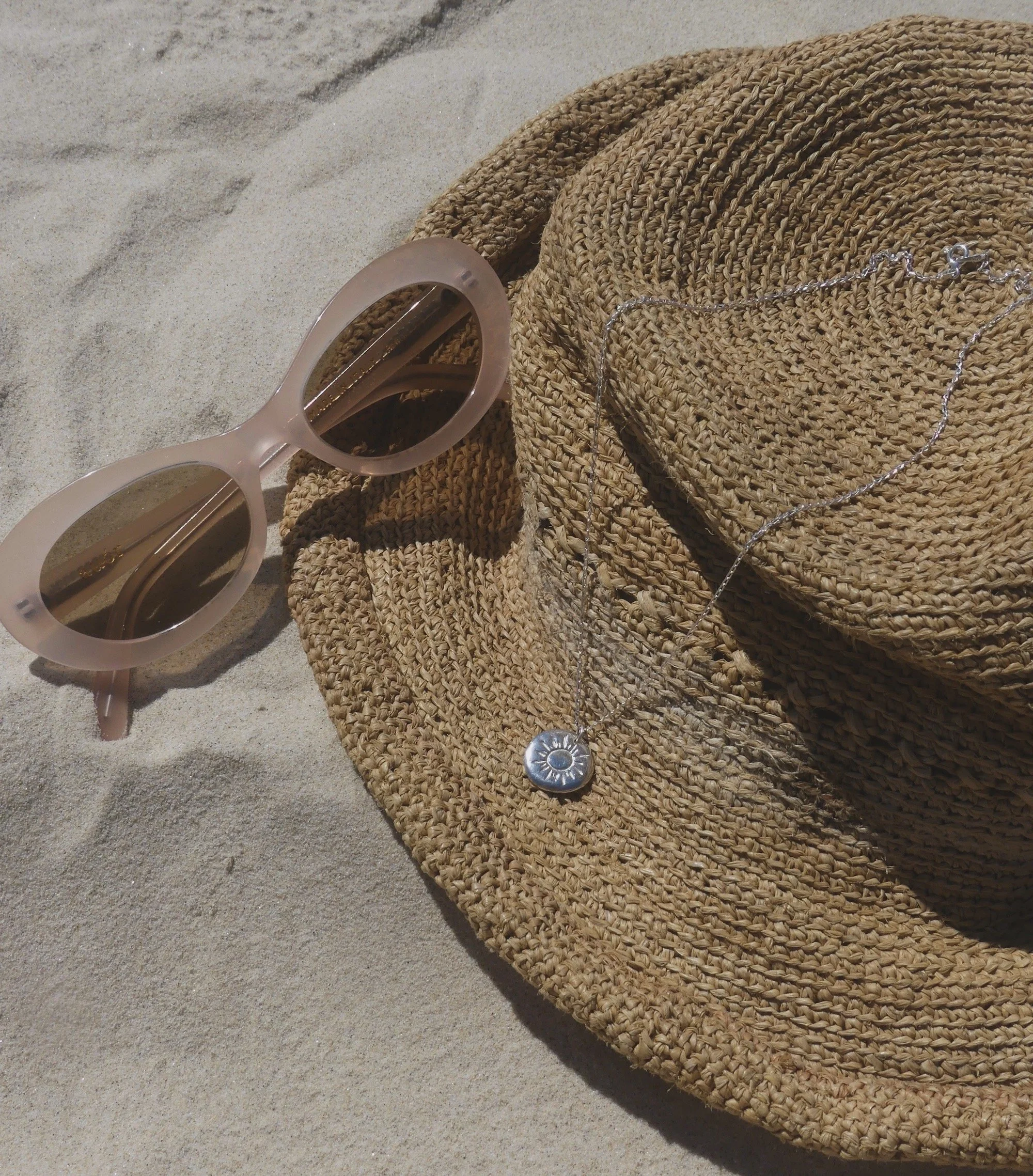 silver sun necklace silver chain with hat and sunglasses on the sand