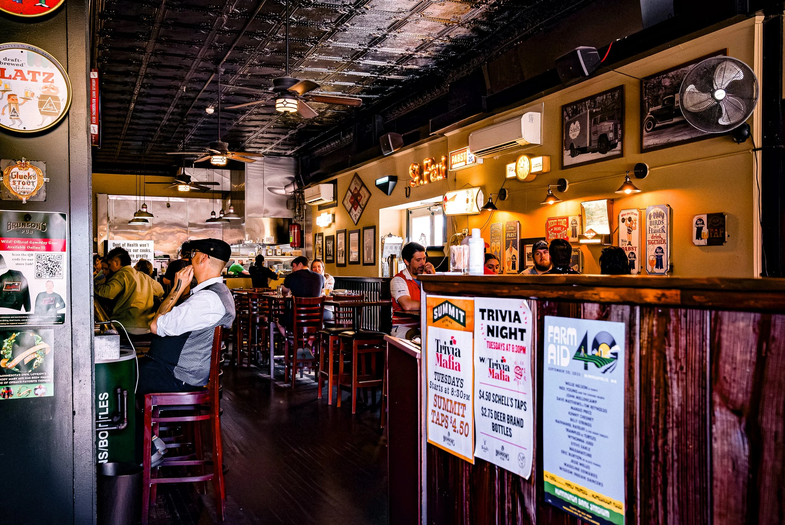 Interior of a casual restaurant with patrons seated at tables, warm lighting, vintage decor, and posters on the walls.