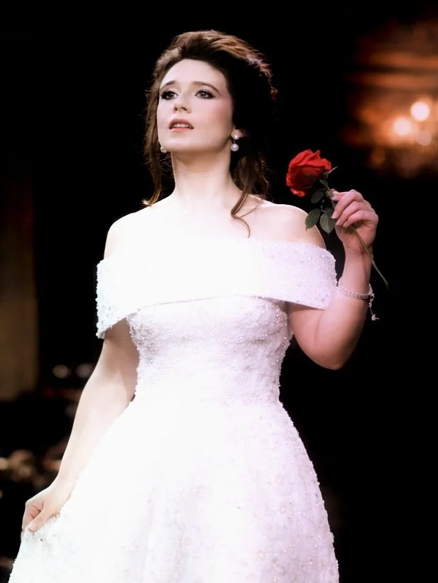 A woman in a white dress holding a red rose.