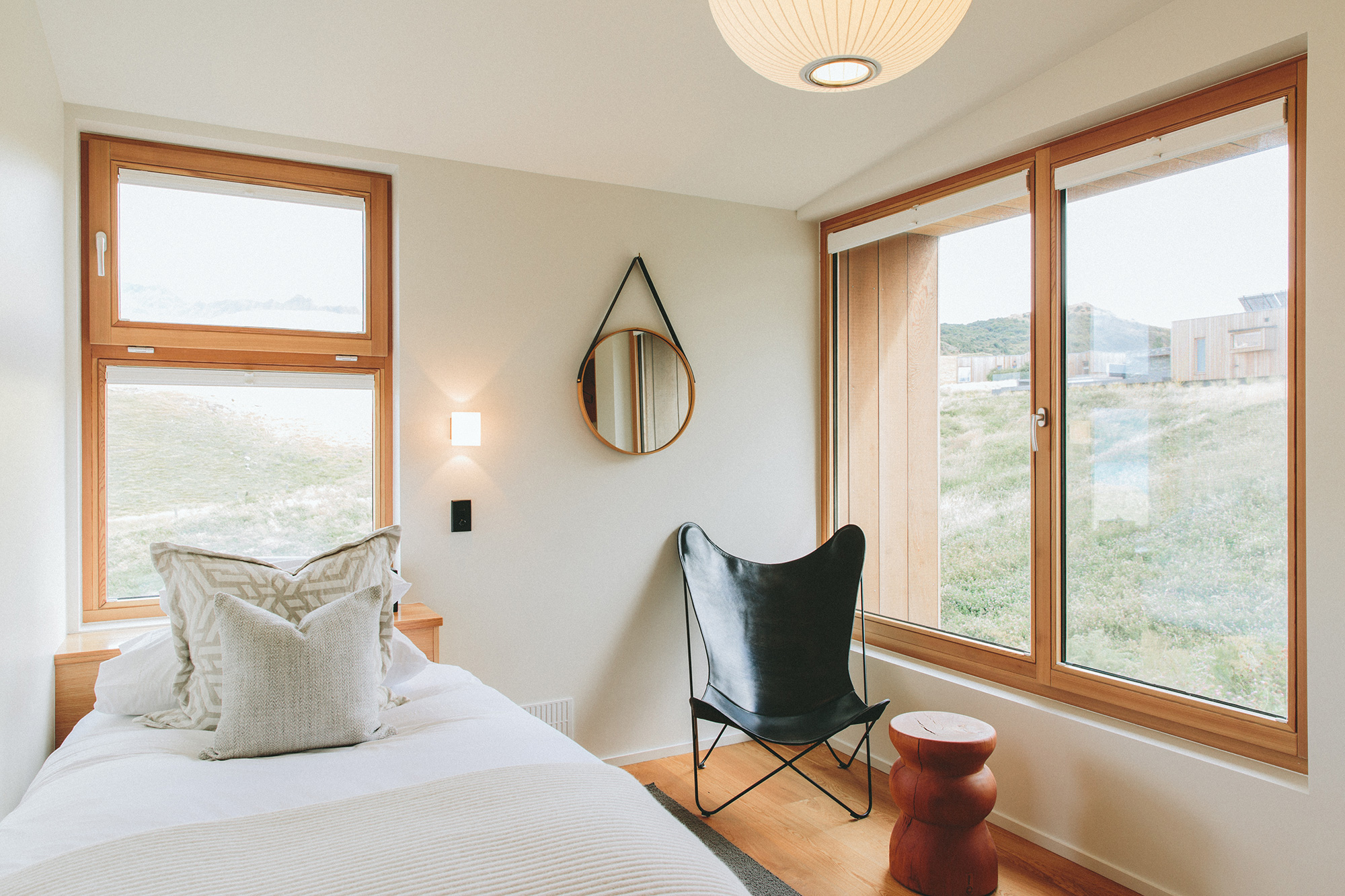  White bed with two gray pillows an windows looking out at a mountain view.  