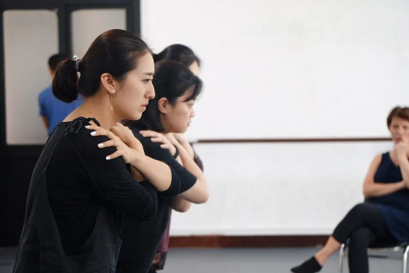 Three participants work on May's 'walk' and sensory awareness in the palms/fingers in Beckett's FOOTFALLS. Their focus is ahead along the path where the 'feet fall', 'indirect', and slightly down emphasizing a looking back within oneself and an opening of one's back awareness.
