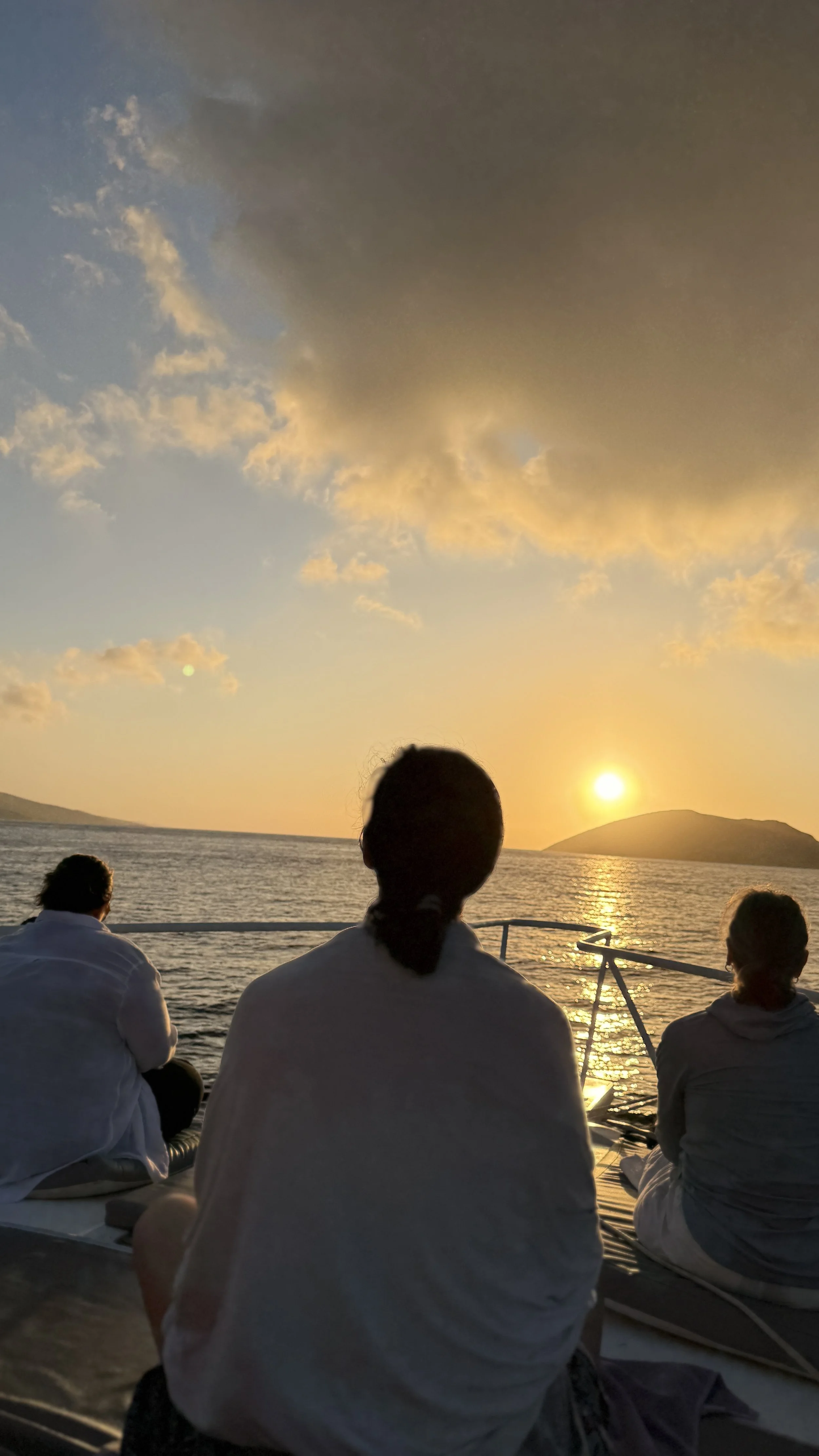 People sitting on a boat watching a sunset over the ocean with a small island in the distance.