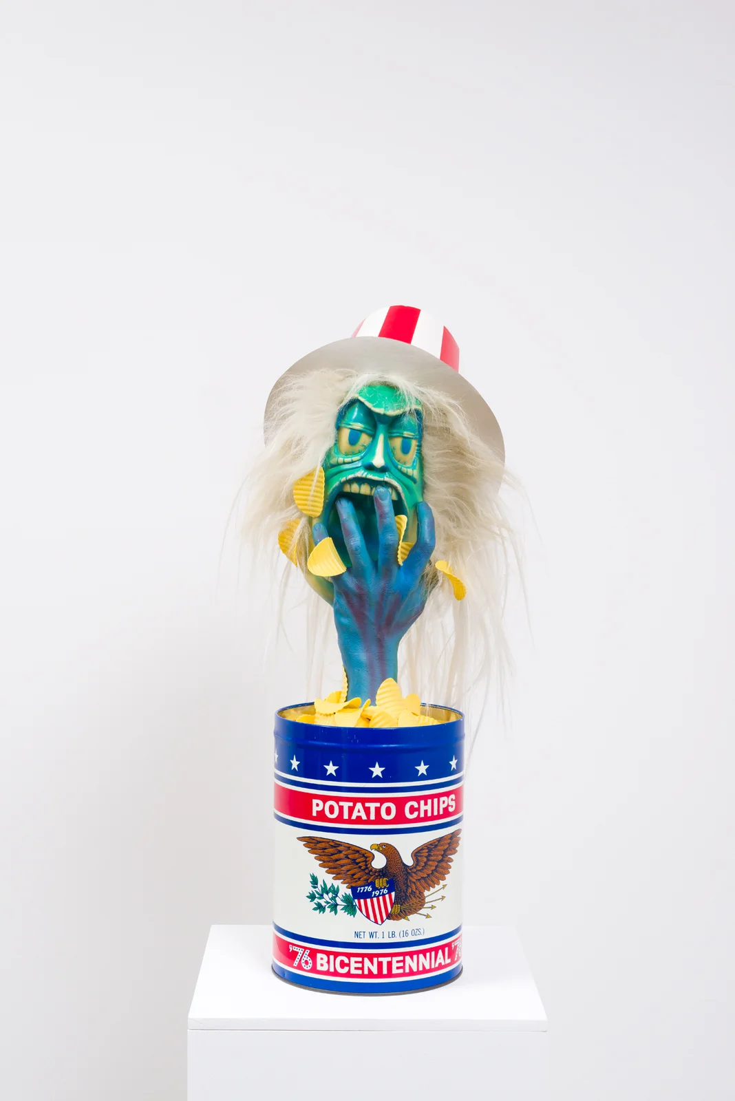 Political Junk Food, 2017 Potato chip tin, plastic potato chips, painted plastic hand and head, wig hair, printed cardboard hat, pedestal