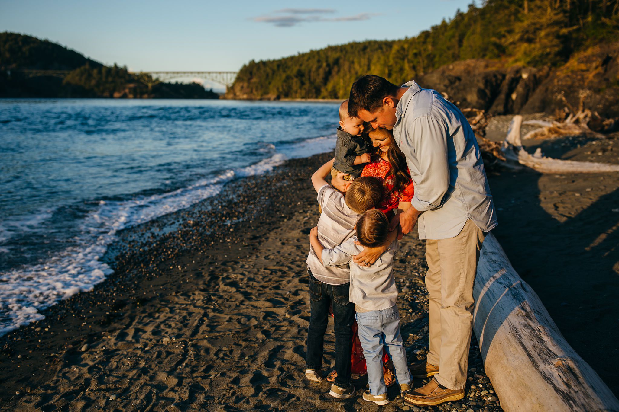 Family hugs on beach with Deception Pass bridge in background