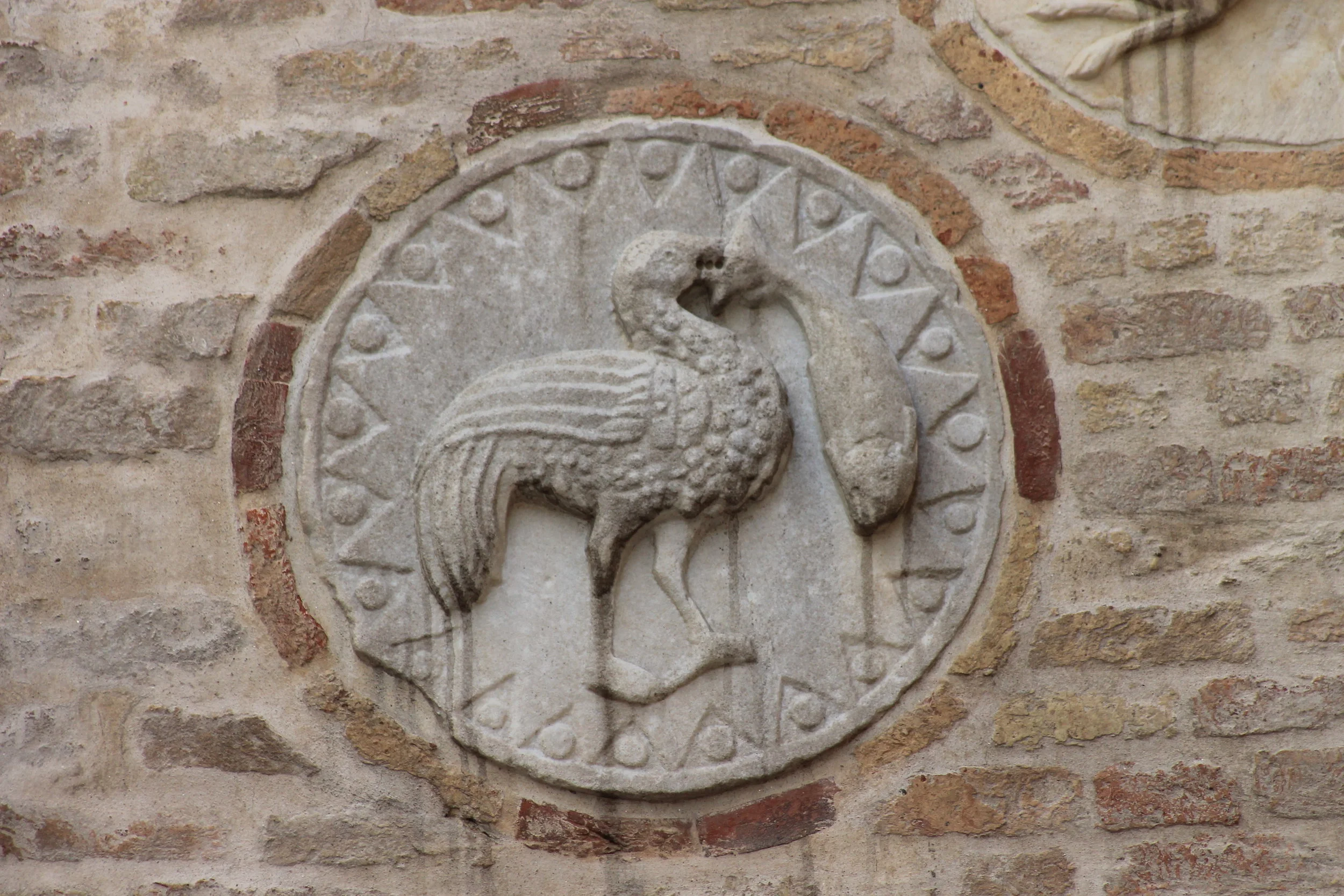 Trampoliere con grosso pesce appeso al becco , altorilievo con bordo a zig-zag e tondini (diam cm. 40 ca.) Marmo greco, XII secolo. Chiesa di Santa Maria del Carmelo, fianco destro del protiro