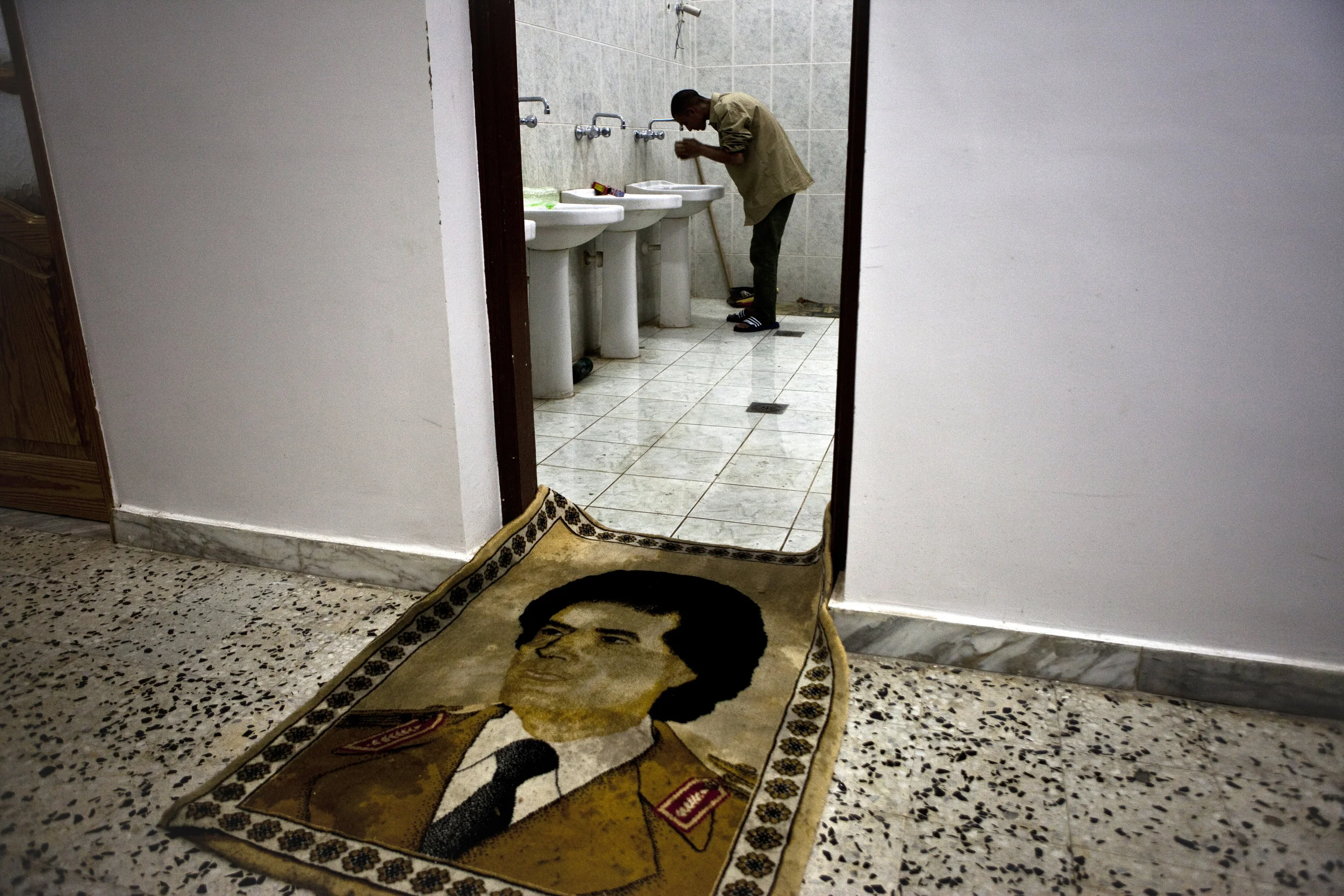  5/10/2011 Misurata, Libya  A captured pro-Qaddafi forces fighter washed before prayer at a rebel detention facility in Misurata, during the siege. A wall tapestry of Col. Qaddafi had been placed as a door-matt for those entering and exiting the rest