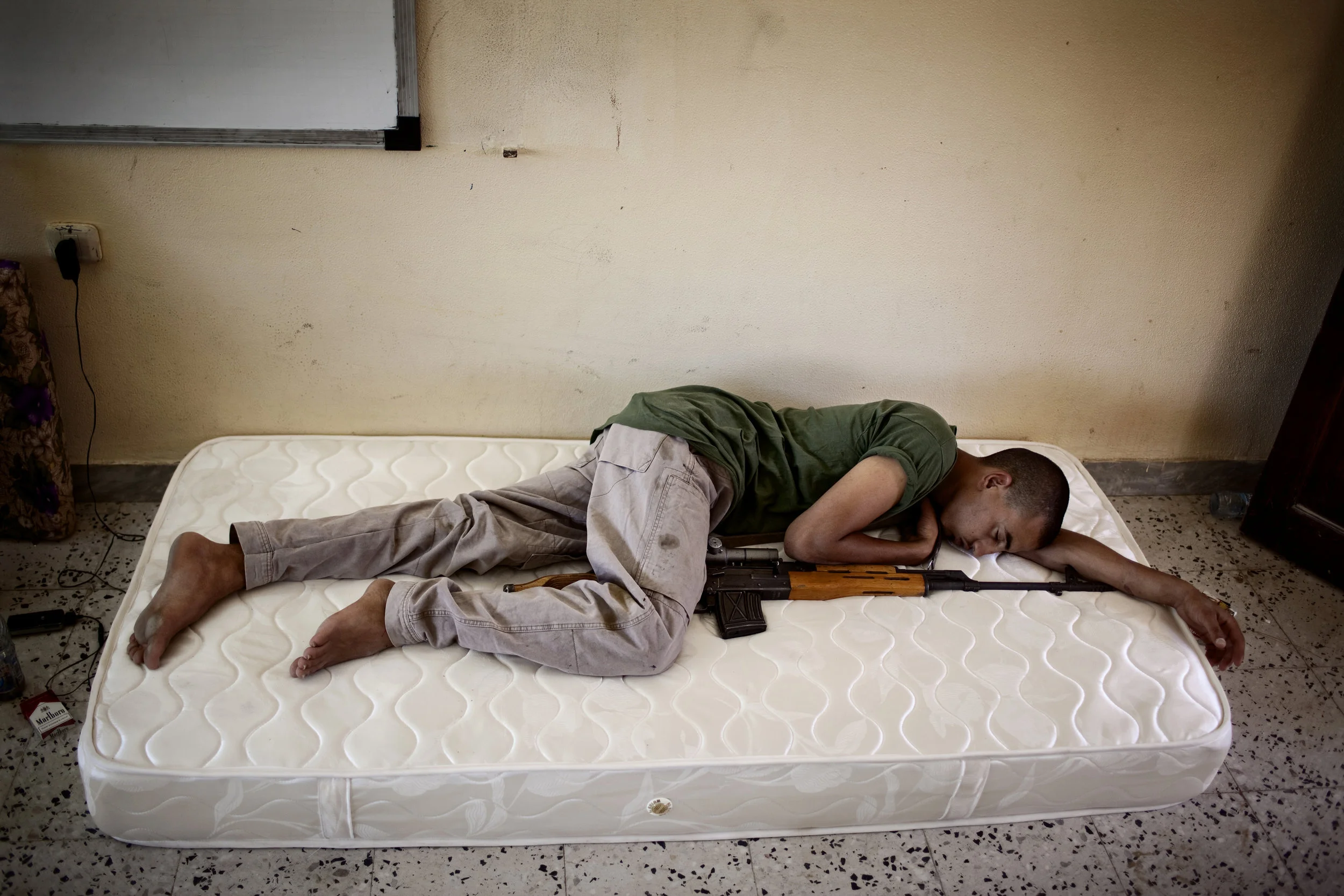  7/5/2011 Kikla, Nafusa Mountains, Libya  A young rebel slept with his sniper rifle at a makeshift rebel military facility in Kikla, during the summer of 2011, when anti-Qaddafi forces were preparing for their final assault on the coastal city of Zaw