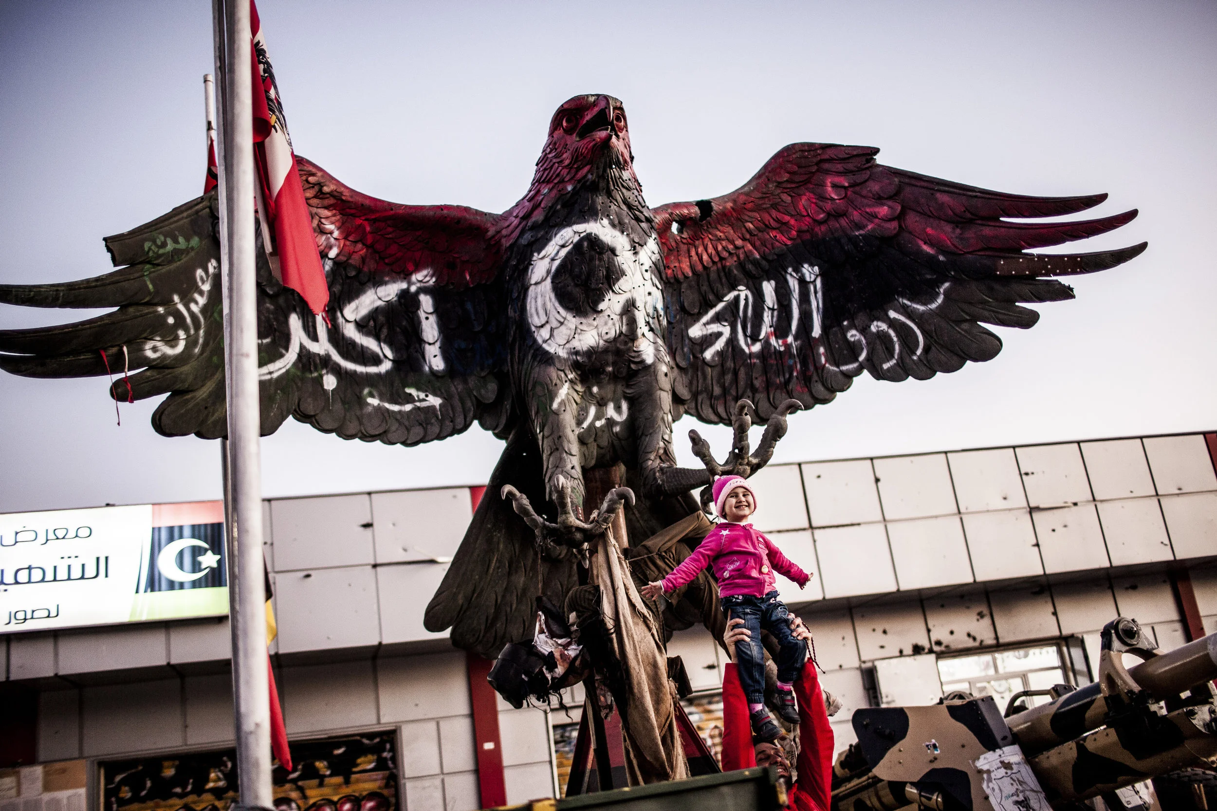  1/27/2012 Misurata, Libya  A young child is held up, under the talons of a large metal sculpture of an eagle that was previously an iconic fixture at Qaddafi's Bab al-Azizia fortress in Tripoli, which the Misurata rebels fought they're way into, loo