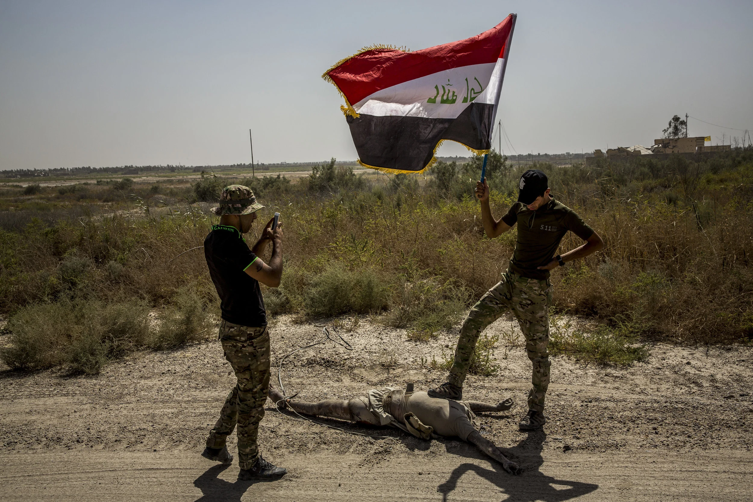  6/27/2016 Fallujah, Iraq  Young members of a Pro-Iraqi government fighting group, one of them carrying an Iraqi flag, stepped on and posed with the dead body of an ISIS fighter that had previously been beheaded and dragged through the streets of Fal