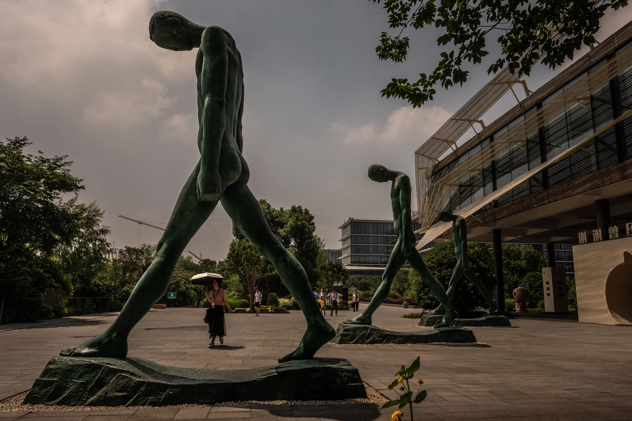 6/1/2018 Hangzhou, China  An employee walked under a sun umbrella, past a series of sculptures, depicting human figures with their heads bowed, at Alibaba Group's main campus in Hangzhou China.  The campus of Alibaba Group in Hangzhou, China. The co