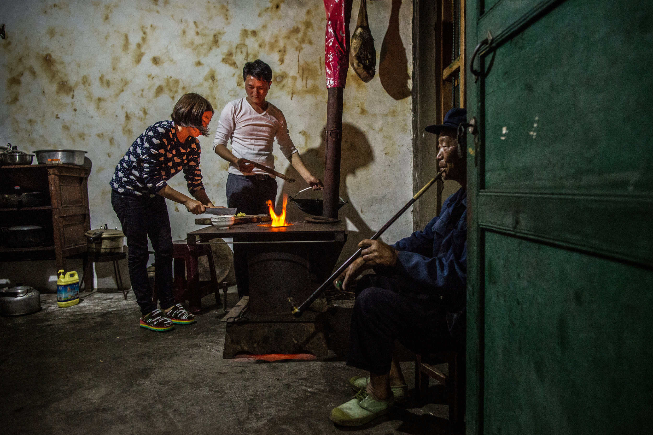  6/14/2017 Zhong He, Guizhou Province, China  Wan Liu, center, one of the managers at the agricultural cooperative, cooked dinner with his wife, as his father smoked a traditional pipe and local tobacco, in the kitchen of the family home. China's rap