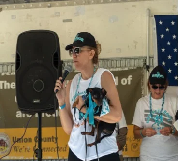 Jill Pall speaks of her cancer story holding her dog, Charlee, in front of marchers in Warinanco Park on September 16. The 5K was hosted by GRACEful Hope, a foundation based in Roselle that aims to raise awareness and funds towards ovarian cancer research. Credit: Facebook.
