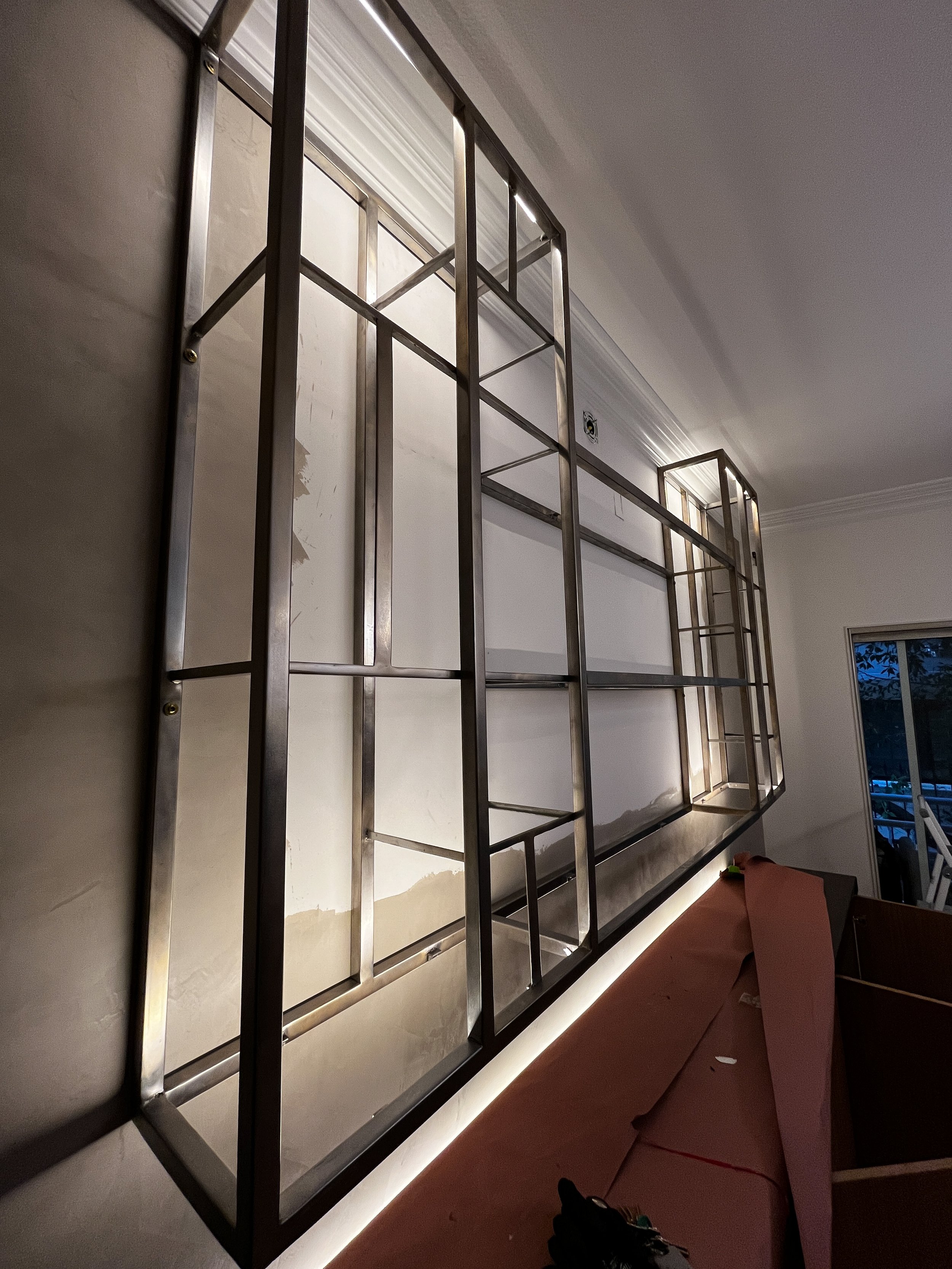 Metal frame wall structure installed on a wall in a room with a sliding glass door, construction materials and tools on a pink work surface.