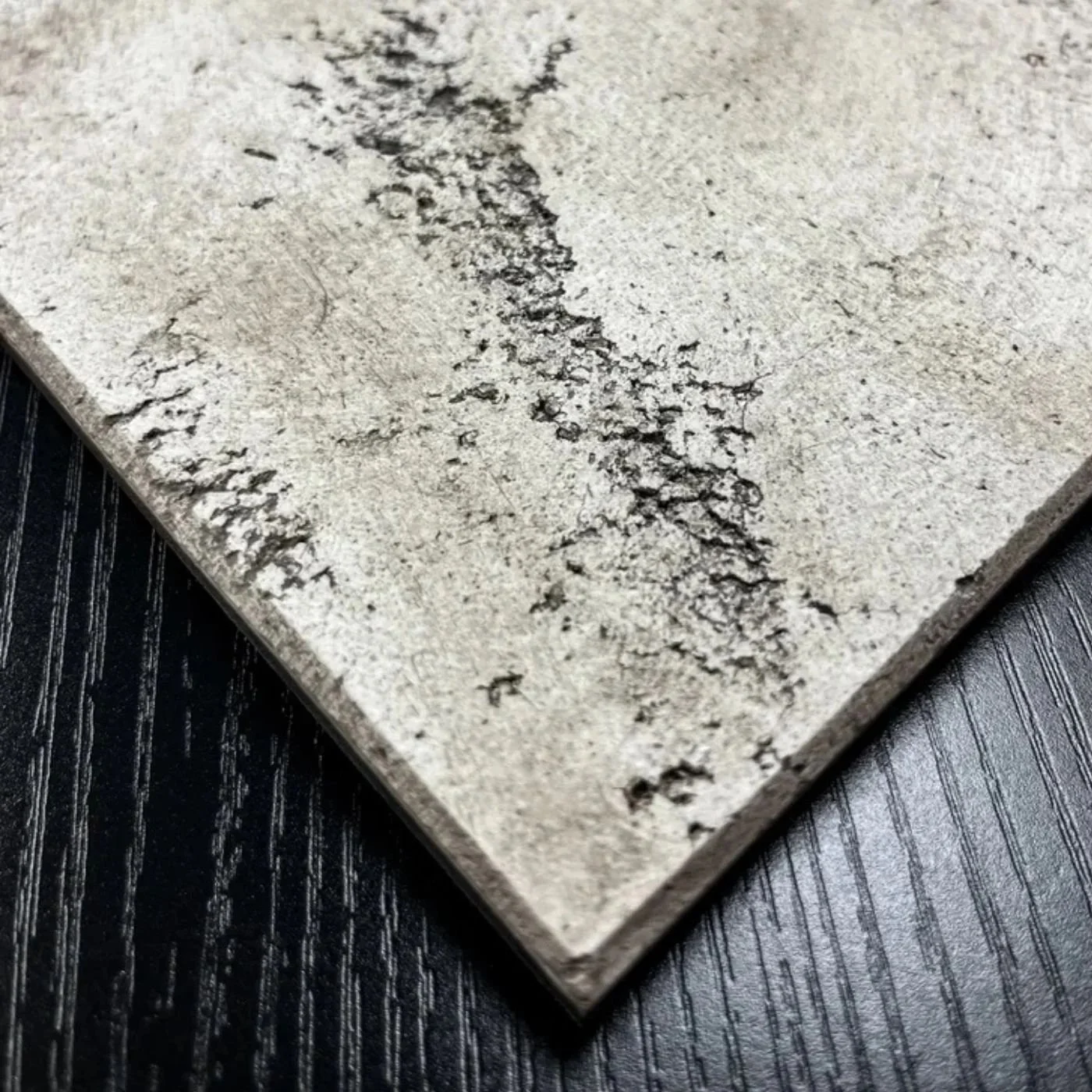 Close-up of a cracked and weathered concrete or stone tile with a textured surface, placed on a black wooden surface.