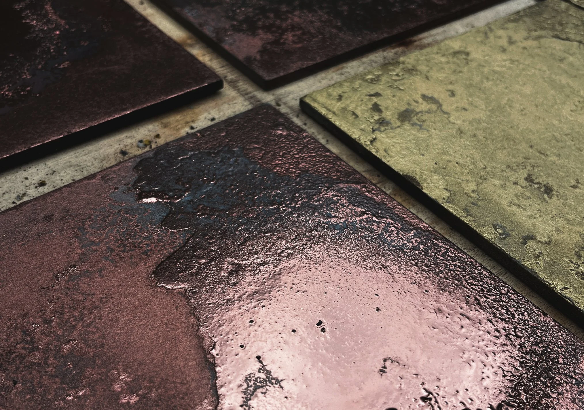 Close-up of multicolored textured tiles, including black, bronze, and greenish-yellow, arranged on a surface.