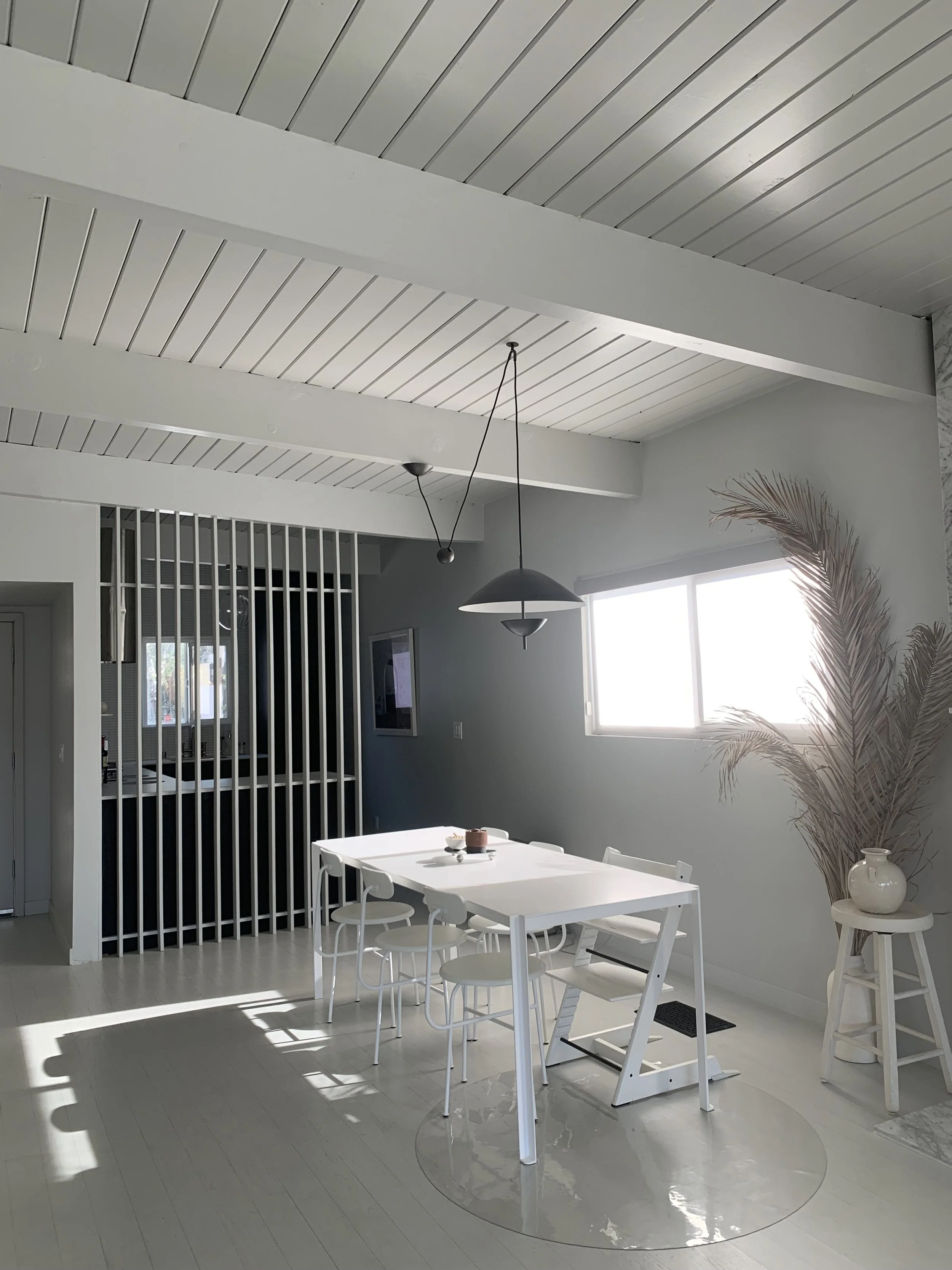 Bright dining area with white table, chairs, and decor, natural light from window, and minimalist design.
