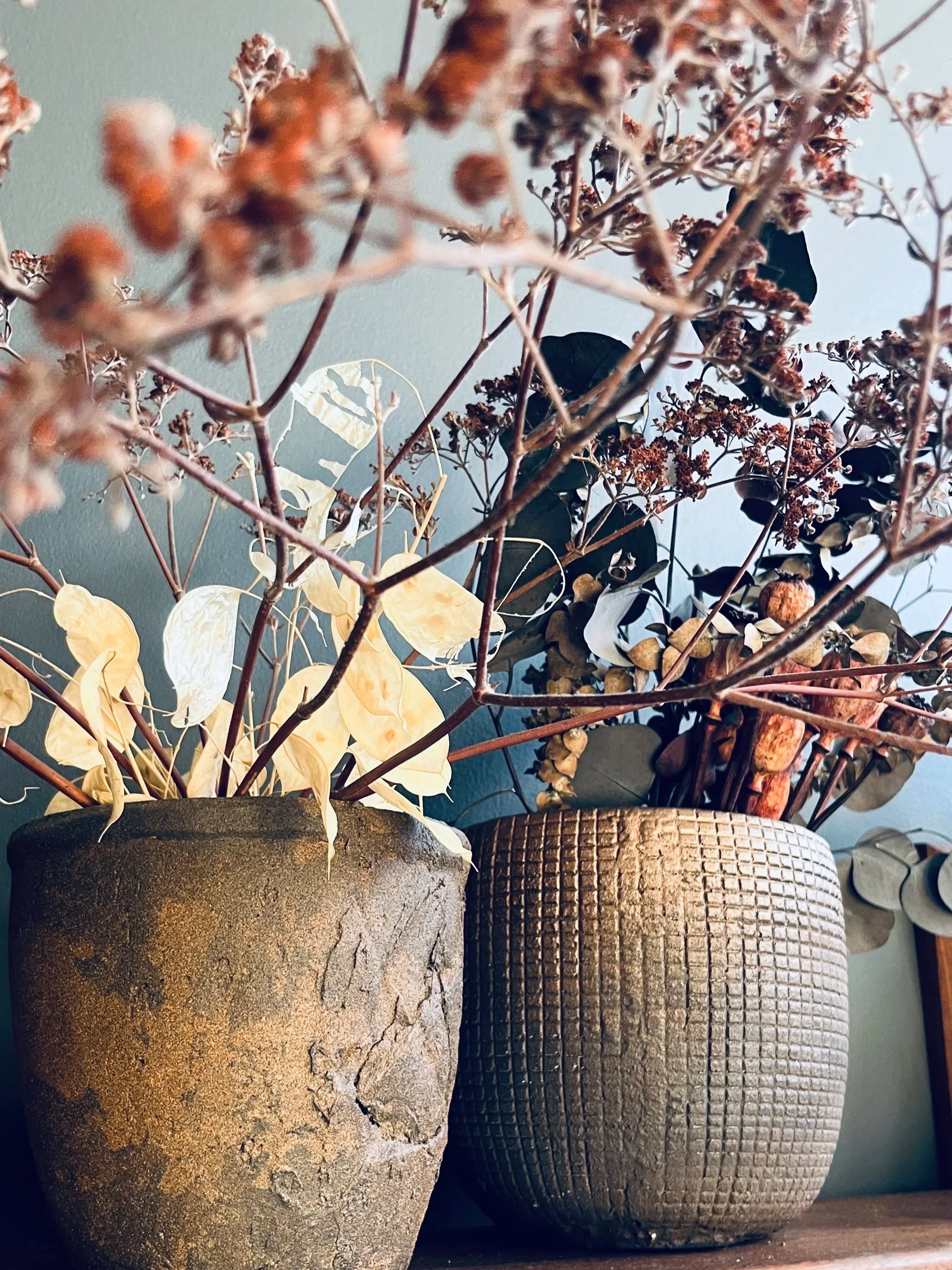Two large rustic vases with dried plants and foliage wabi sabi hand patina vases decor hospitality design.