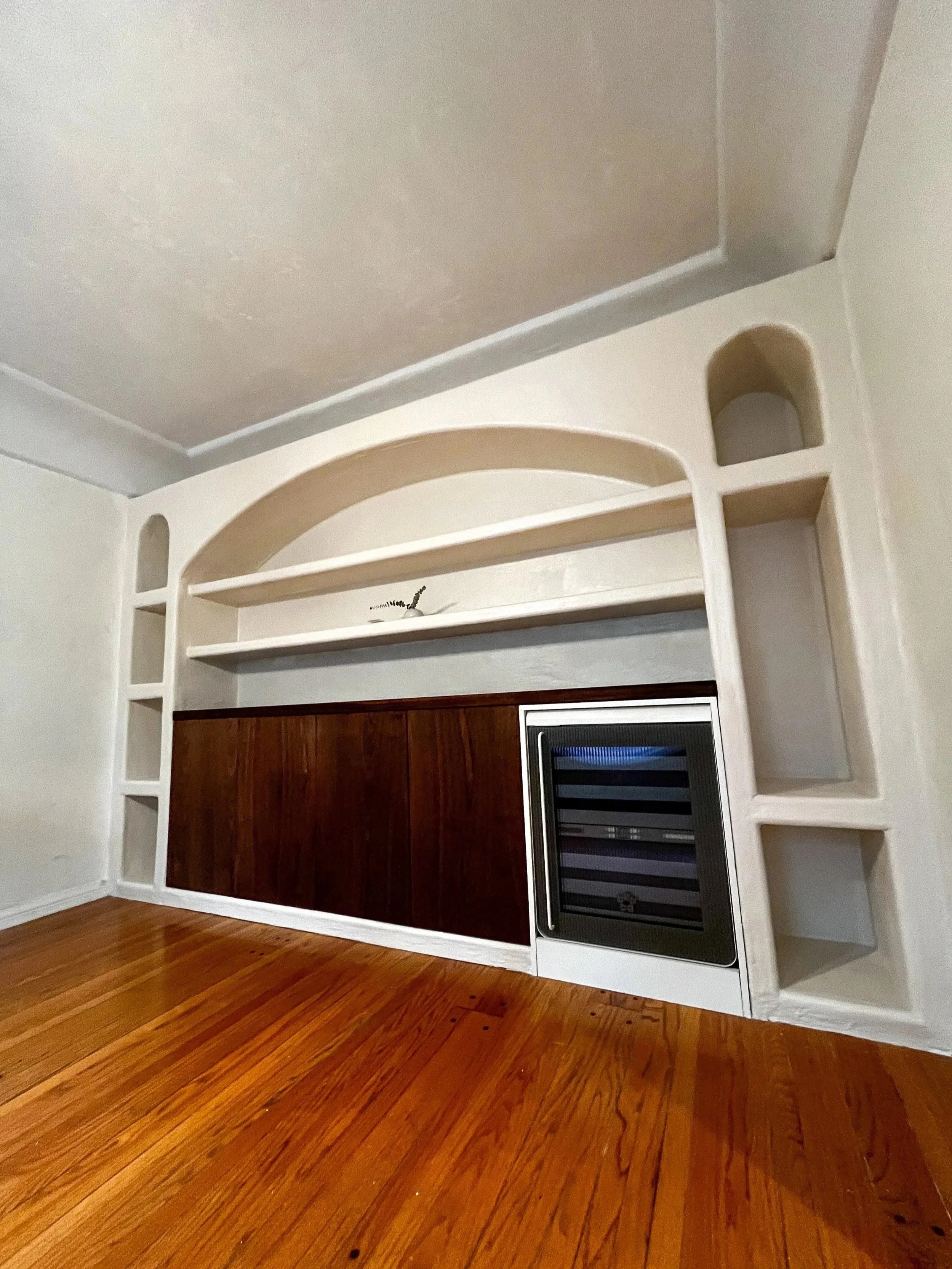 Built-in entertainment center with shelves, cabinets, and a wine cooler on a wooden floor.