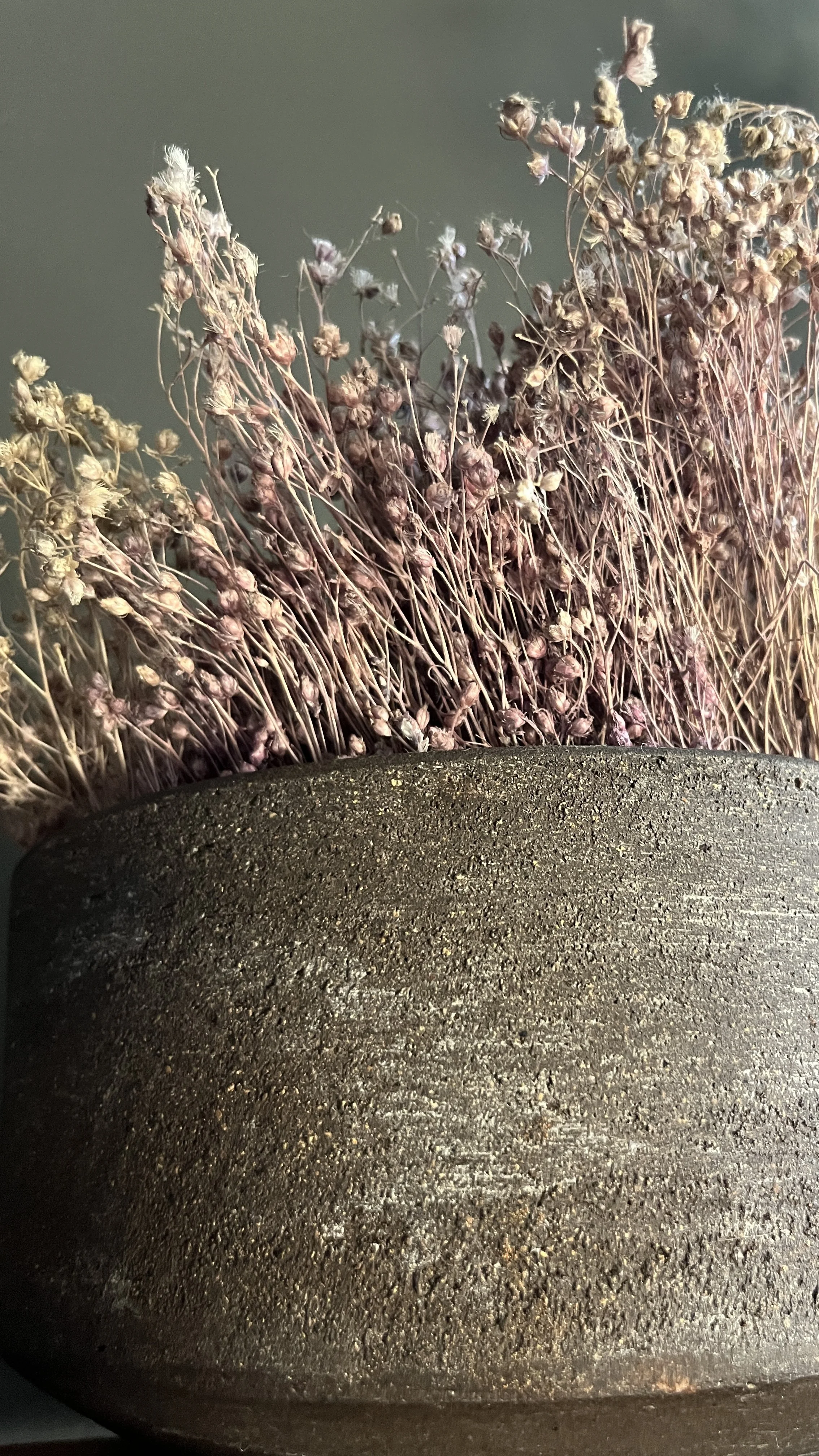 A textured black ceramic vase holding dried pink and beige flowers