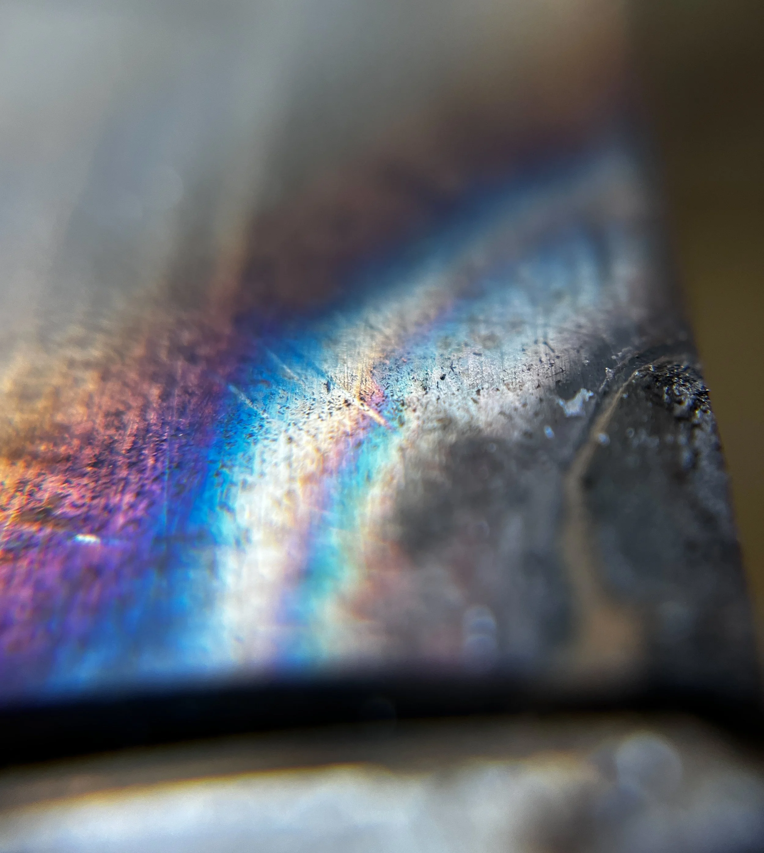 Close-up of a metal surface with rainbow-colored light reflection and some surface texture.