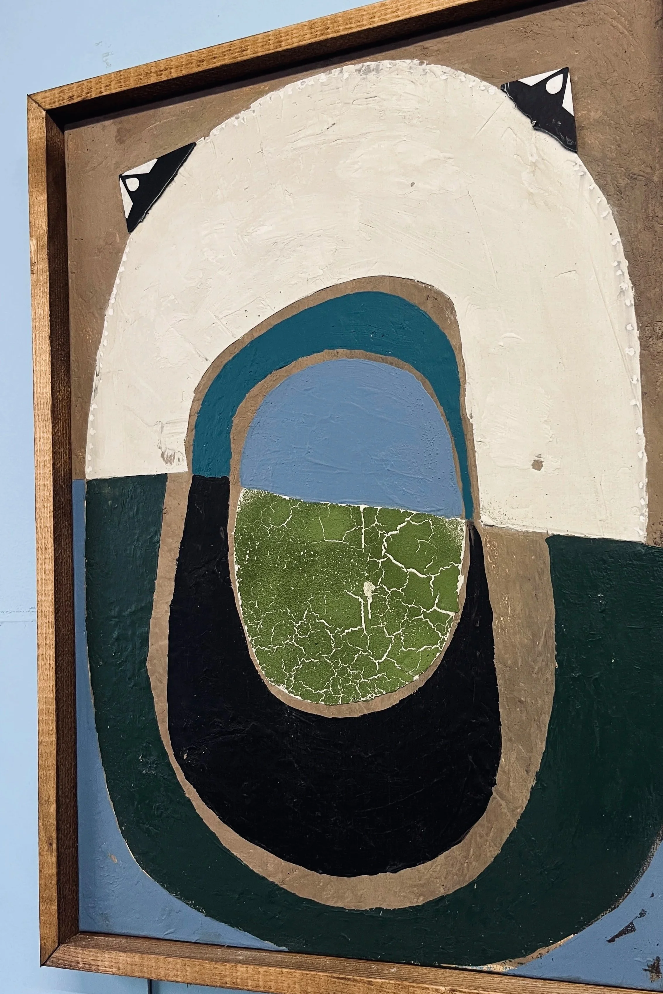 Abstract painting with layered geometric shapes and bold colors, including white, blue, green, black, and tan, on a wooden framed canvas.