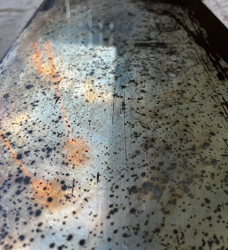 Close-up of a metallic surface with numerous black and orange rust spots and streaks.