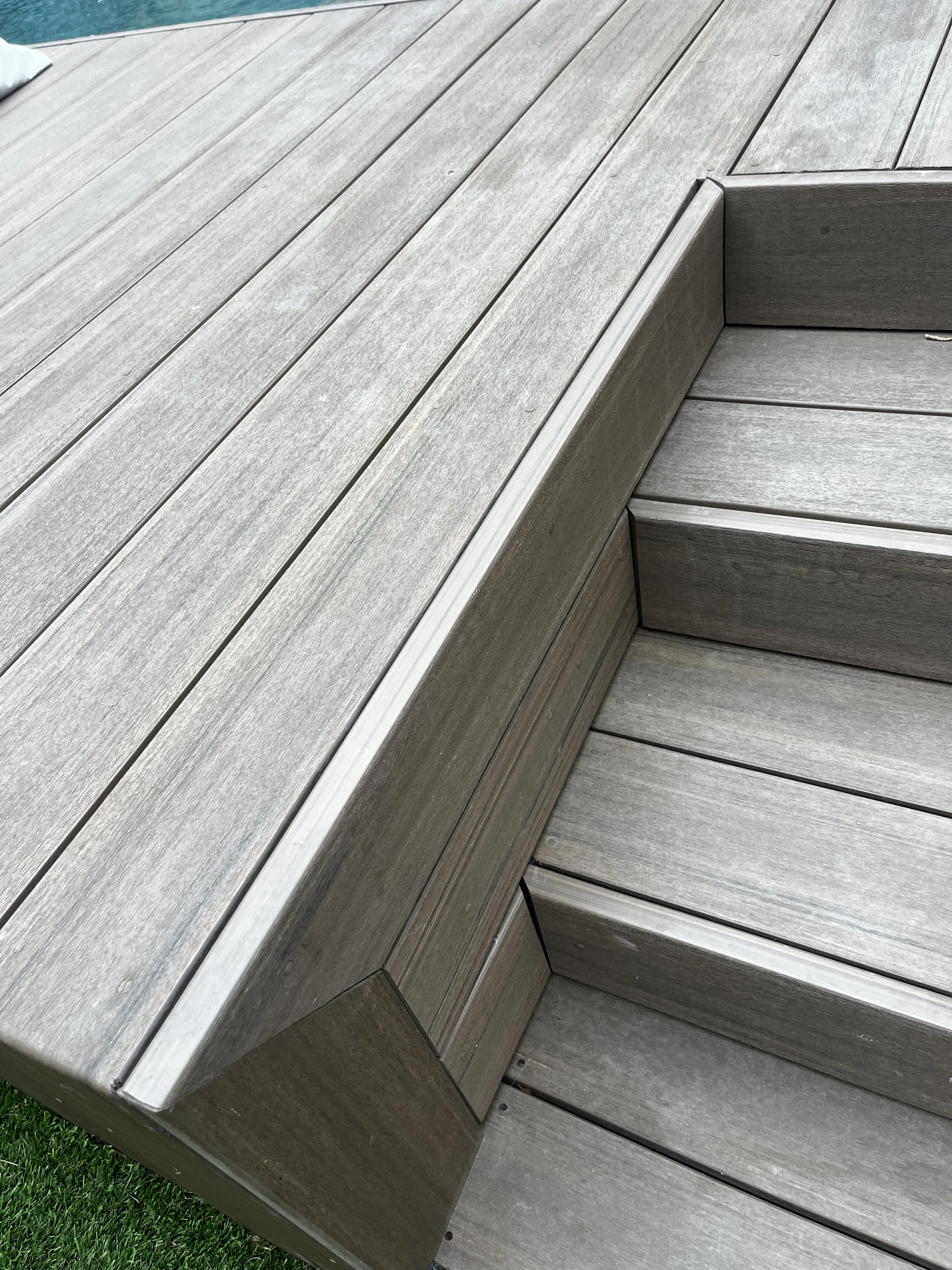 Close-up of gray wooden outdoor steps with a section of wooden deck and grass visible at the edge.