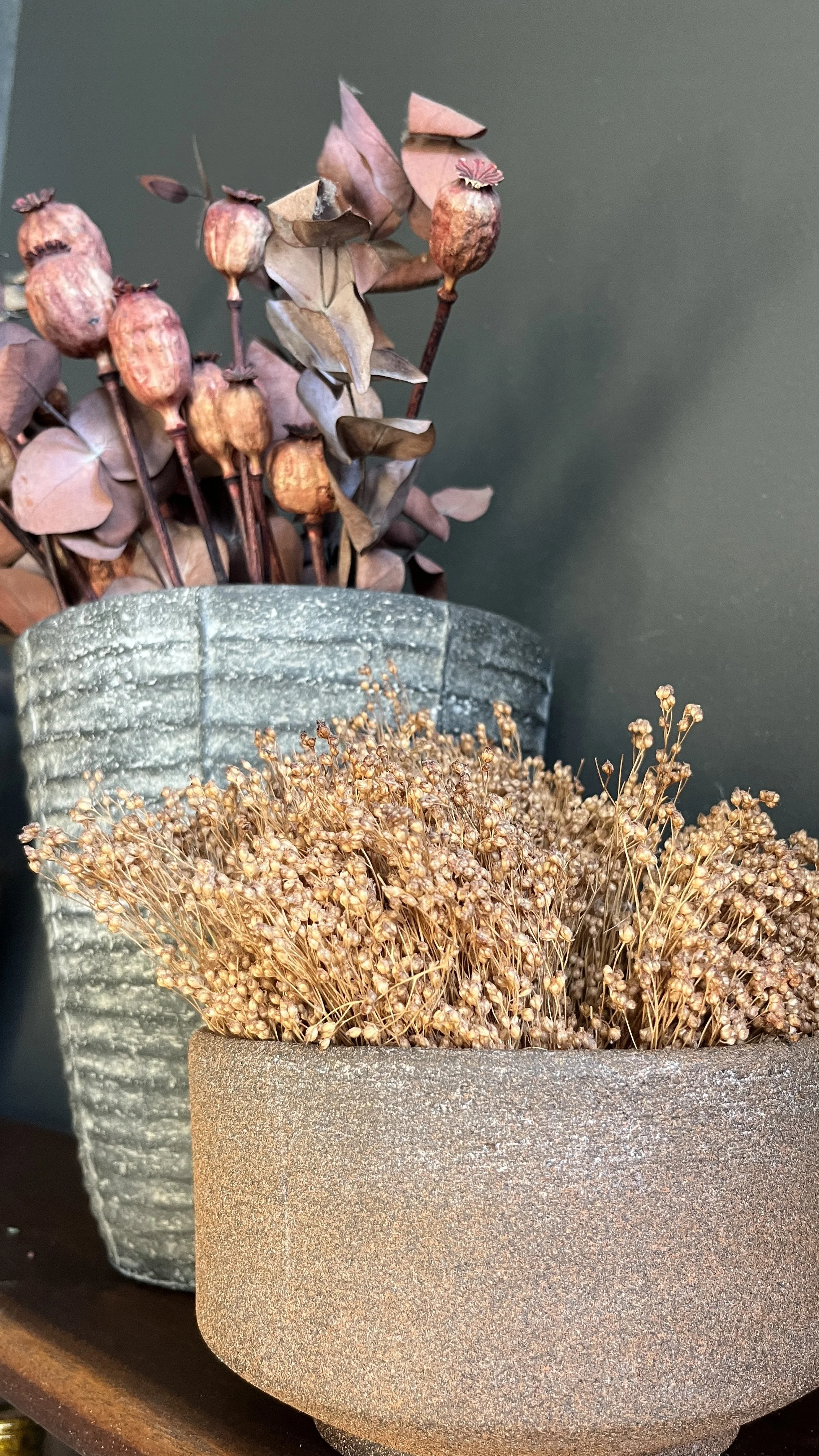 Two textured, gray and terra cotta colored planters with dried flowers, set against a dark background.
