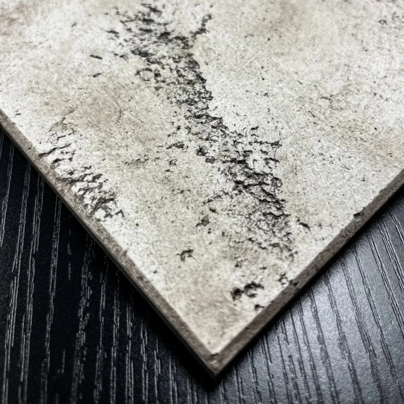 Close-up of a gray concrete or stone tile with dark veins and texture, placed on a black wooden surface.
