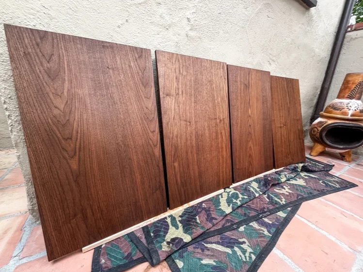 Four wooden panels leaning against a wall, with a camouflage-patterned fabric and a shoe-shaped decorative item on the tiles nearby.