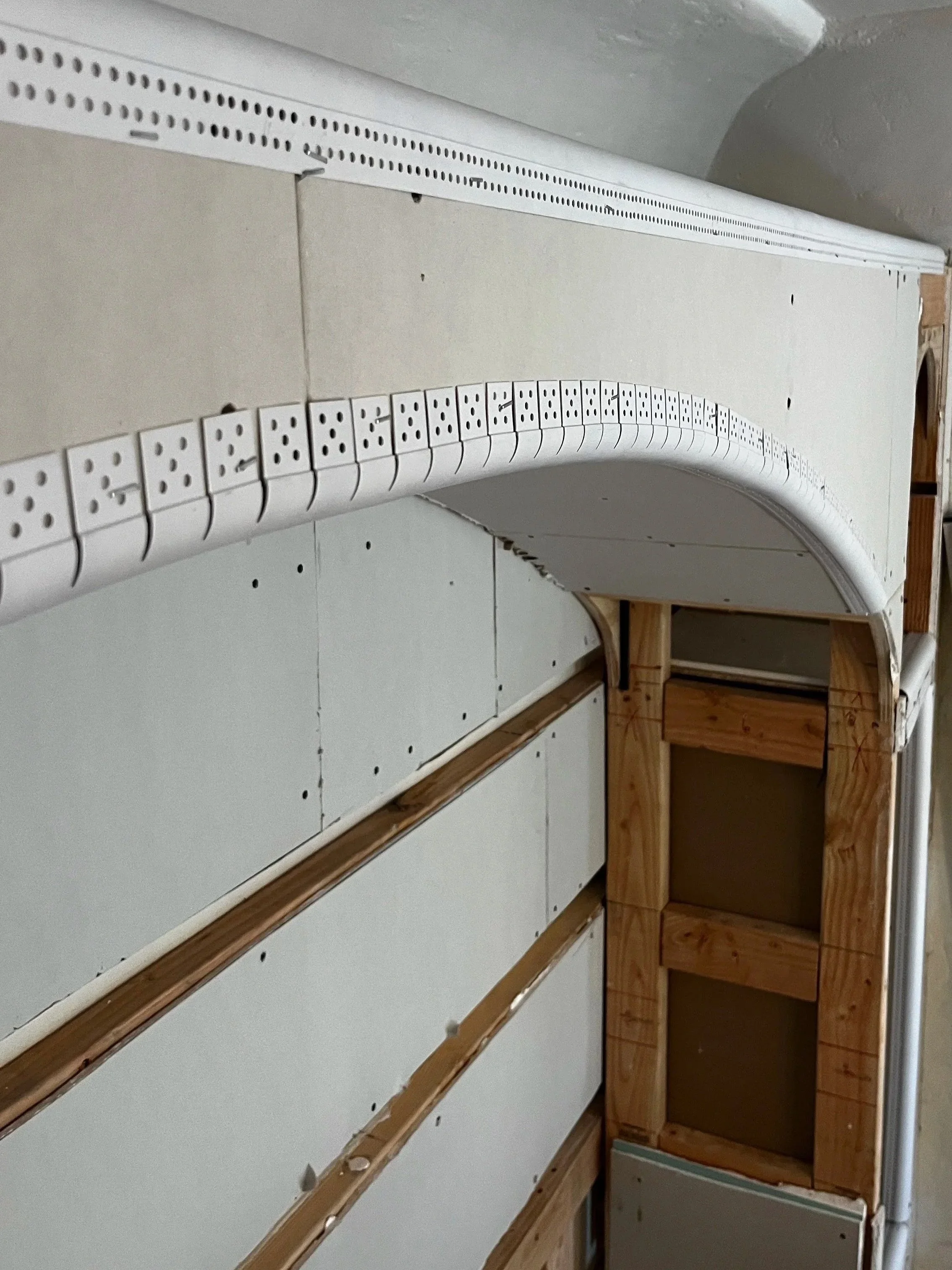 Interior view of an unfinished wall with drywall and electrical wiring, including a curved white cable management system and wooden framing.