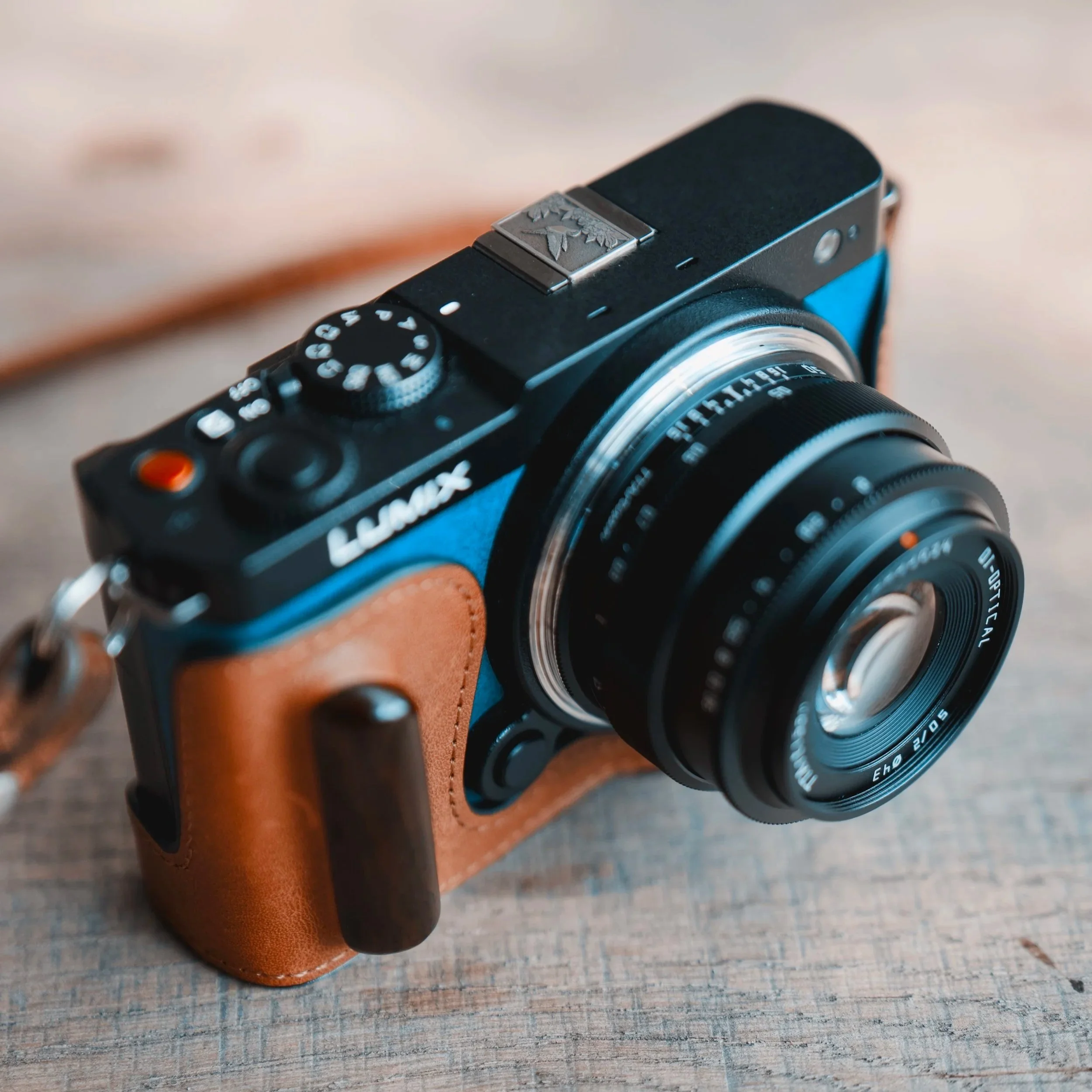 A digital camera resting on a large log in a forest with autumn-colored trees and a river in the background.