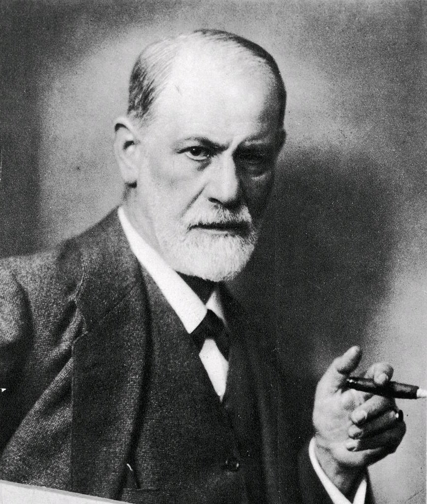 Black and white portrait of an elderly man with a beard and mustache holding a cigar in his right hand, looking directly at the camera, wearing a suit and tie.
