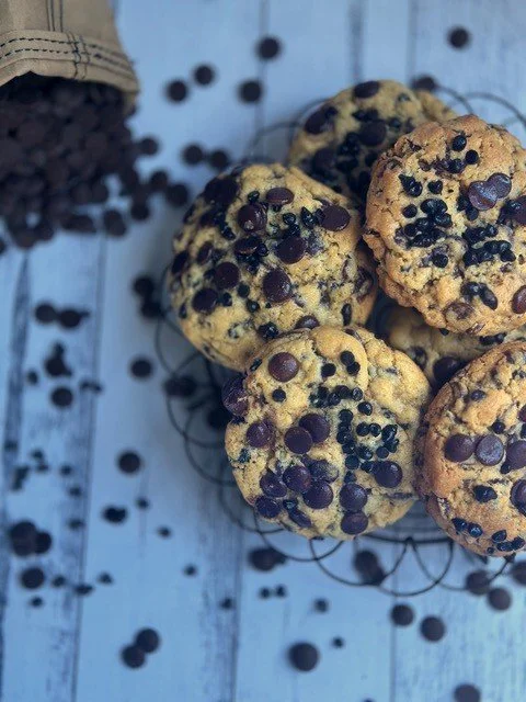 Freshly baked chocolate chip cookies on a wire cooling rack with scattered chocolate chips on a blue wooden surface